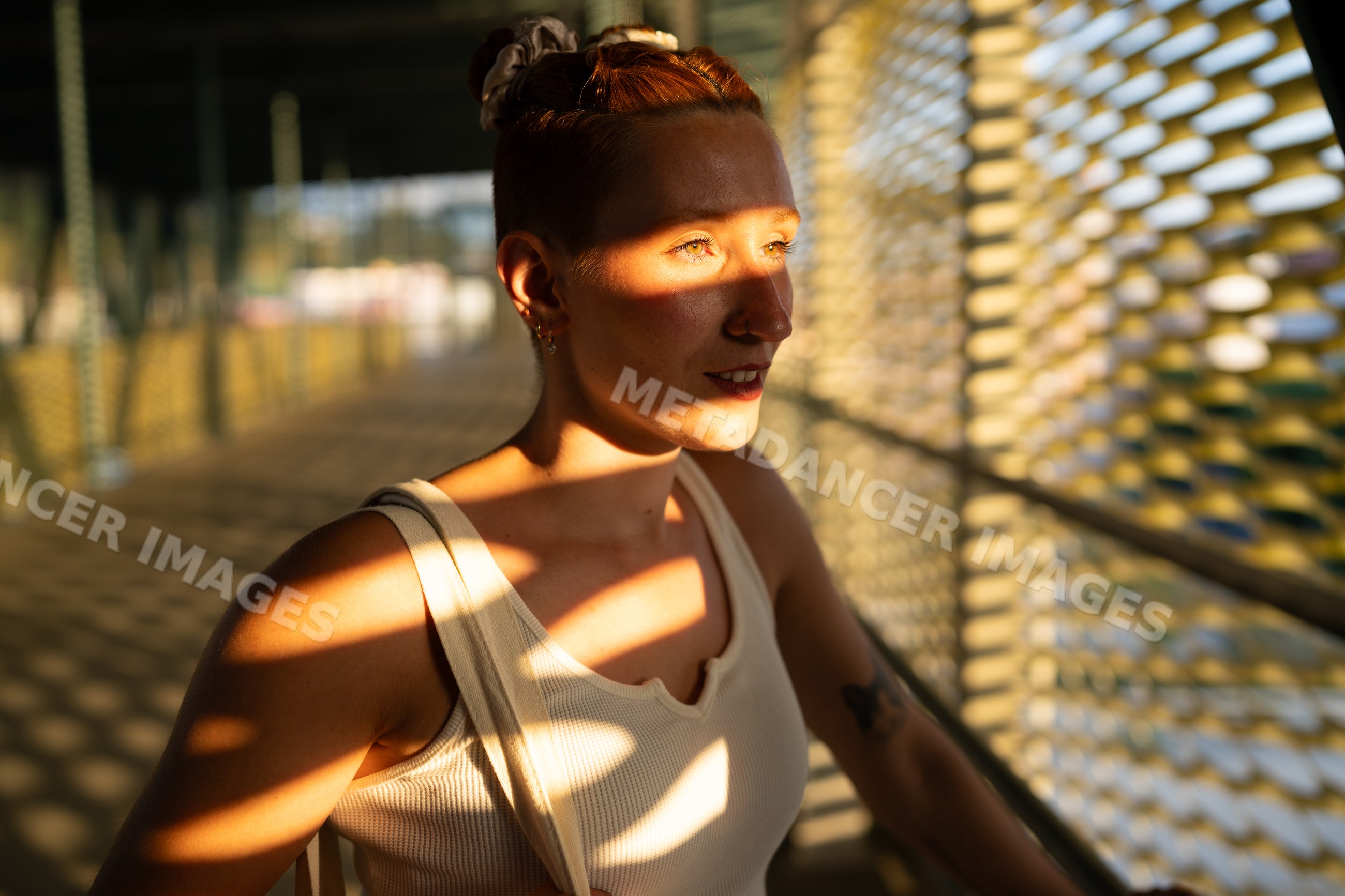 A white woman stands in sunlight and shadow on an urban bridge