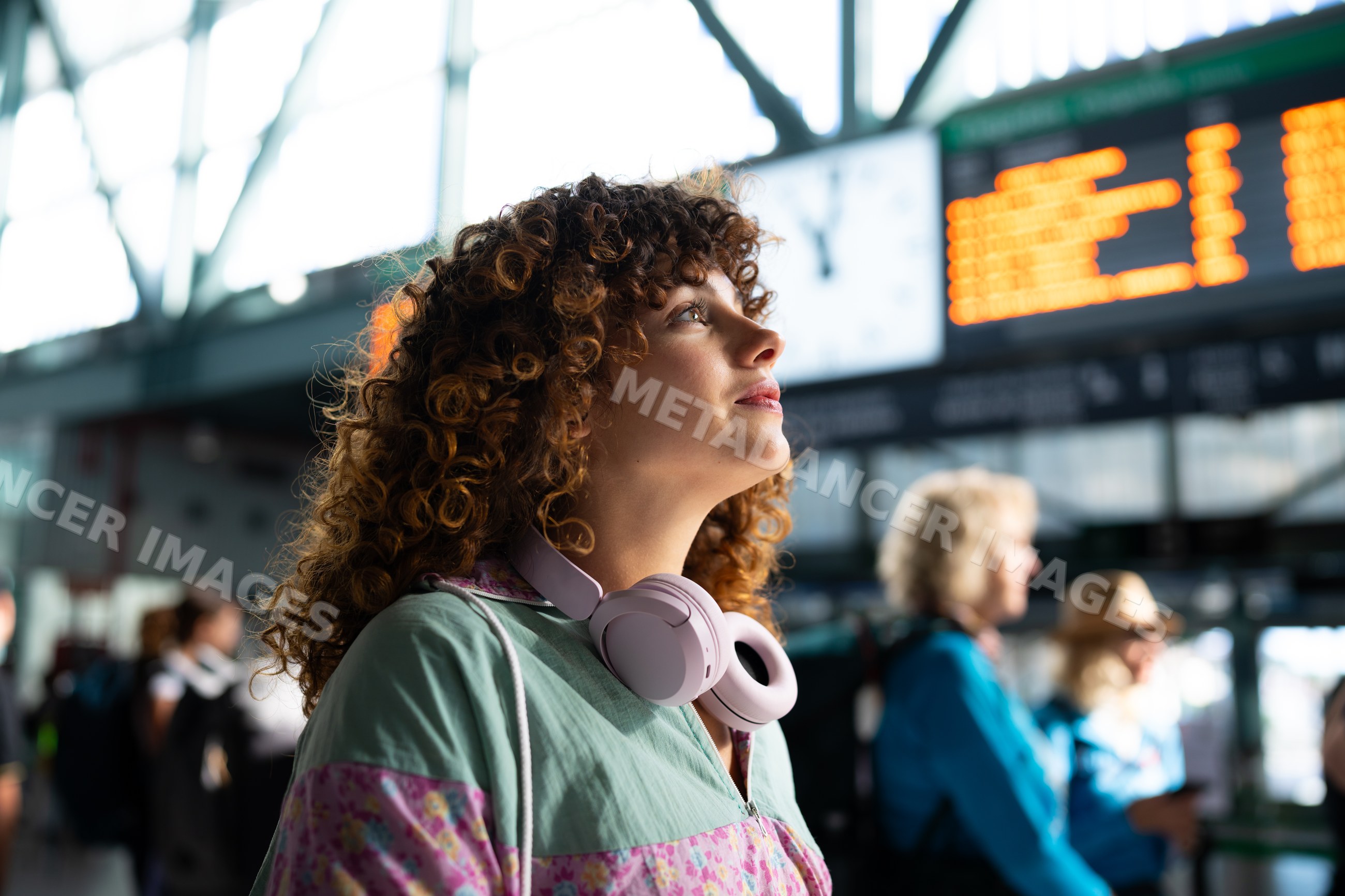 White woman with headphones looking at train arrival board in station