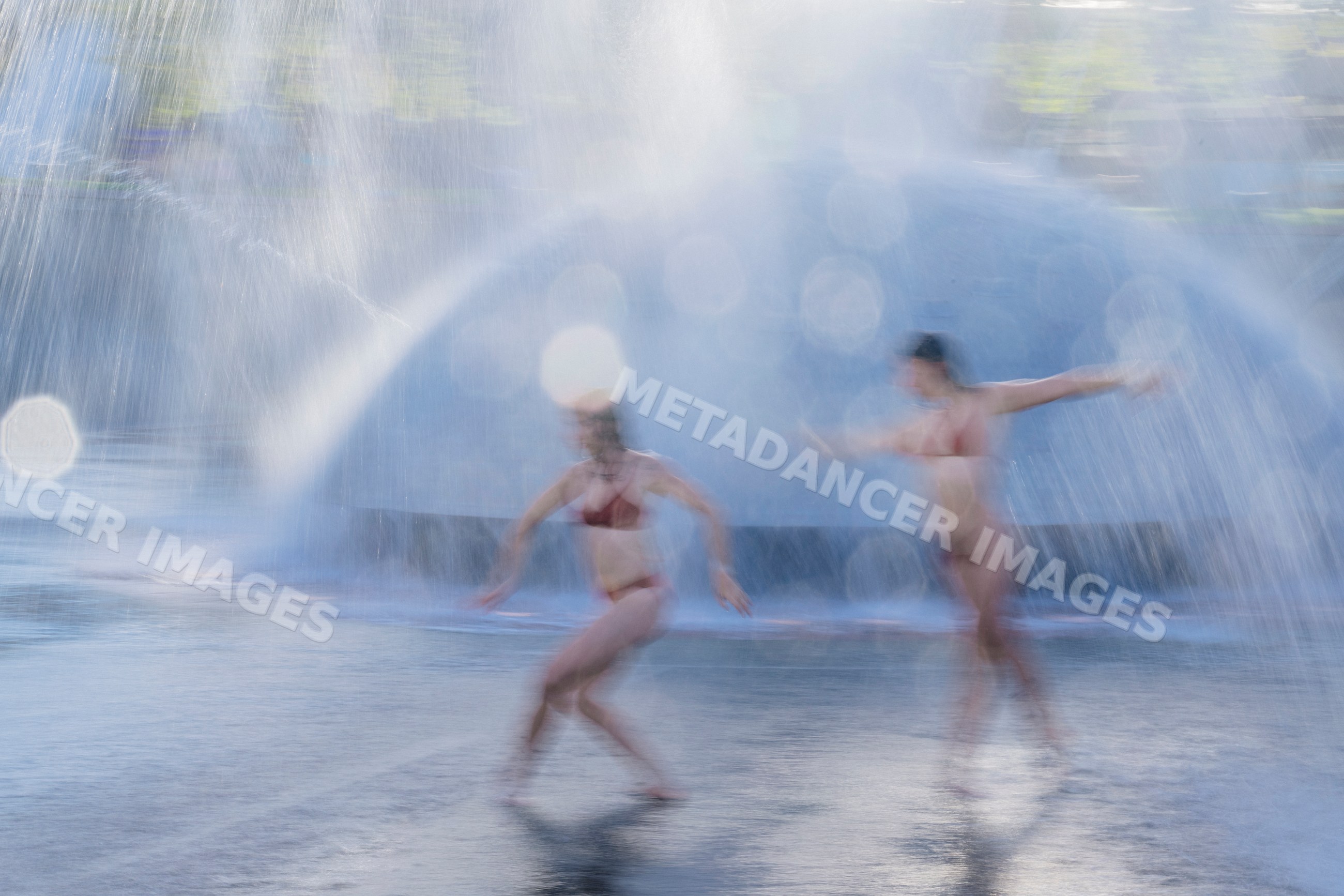 White women dancing dynamically through water fountain spray outdoors