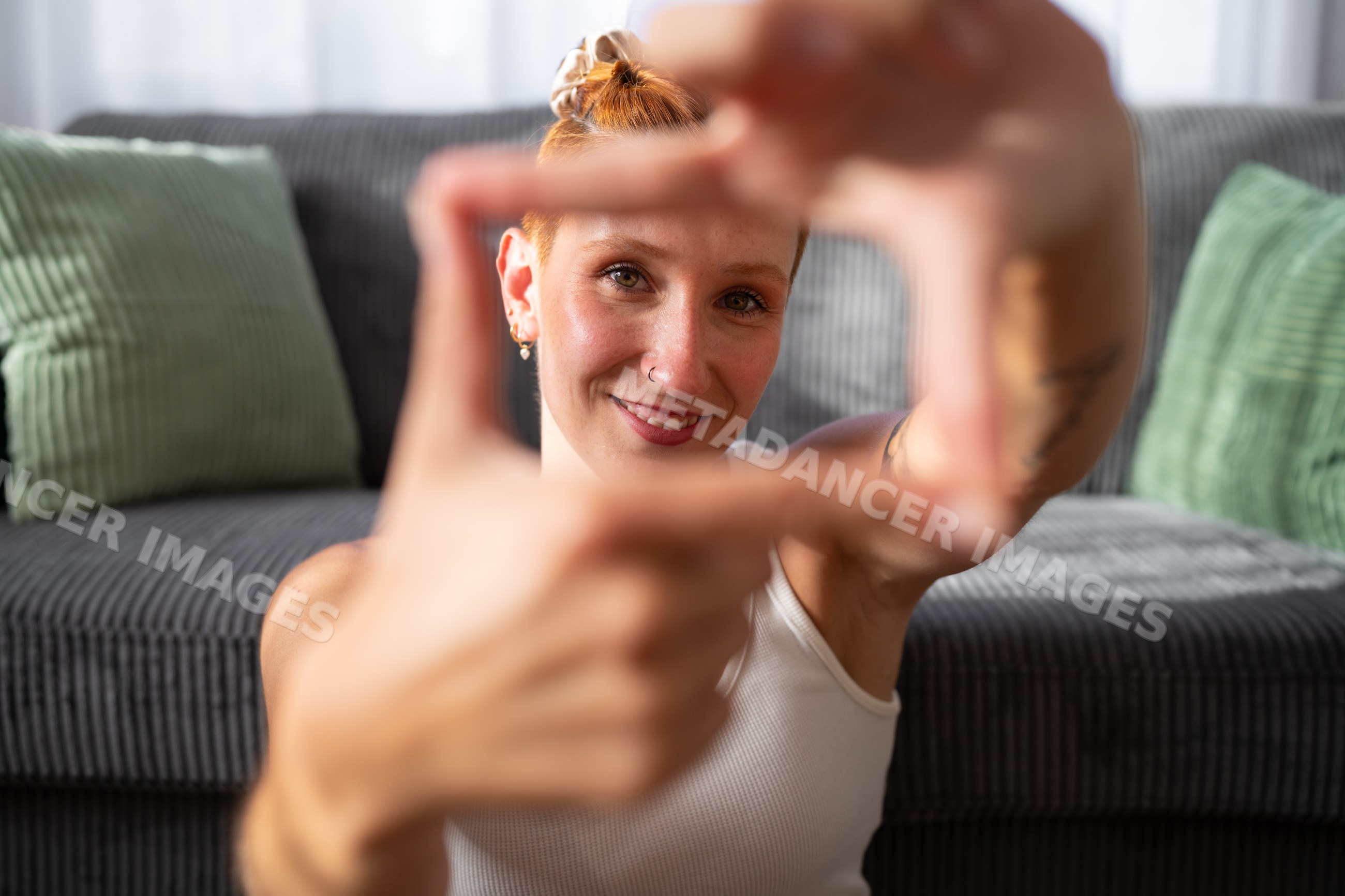 A white woman makes a hand frame and smiles indoors