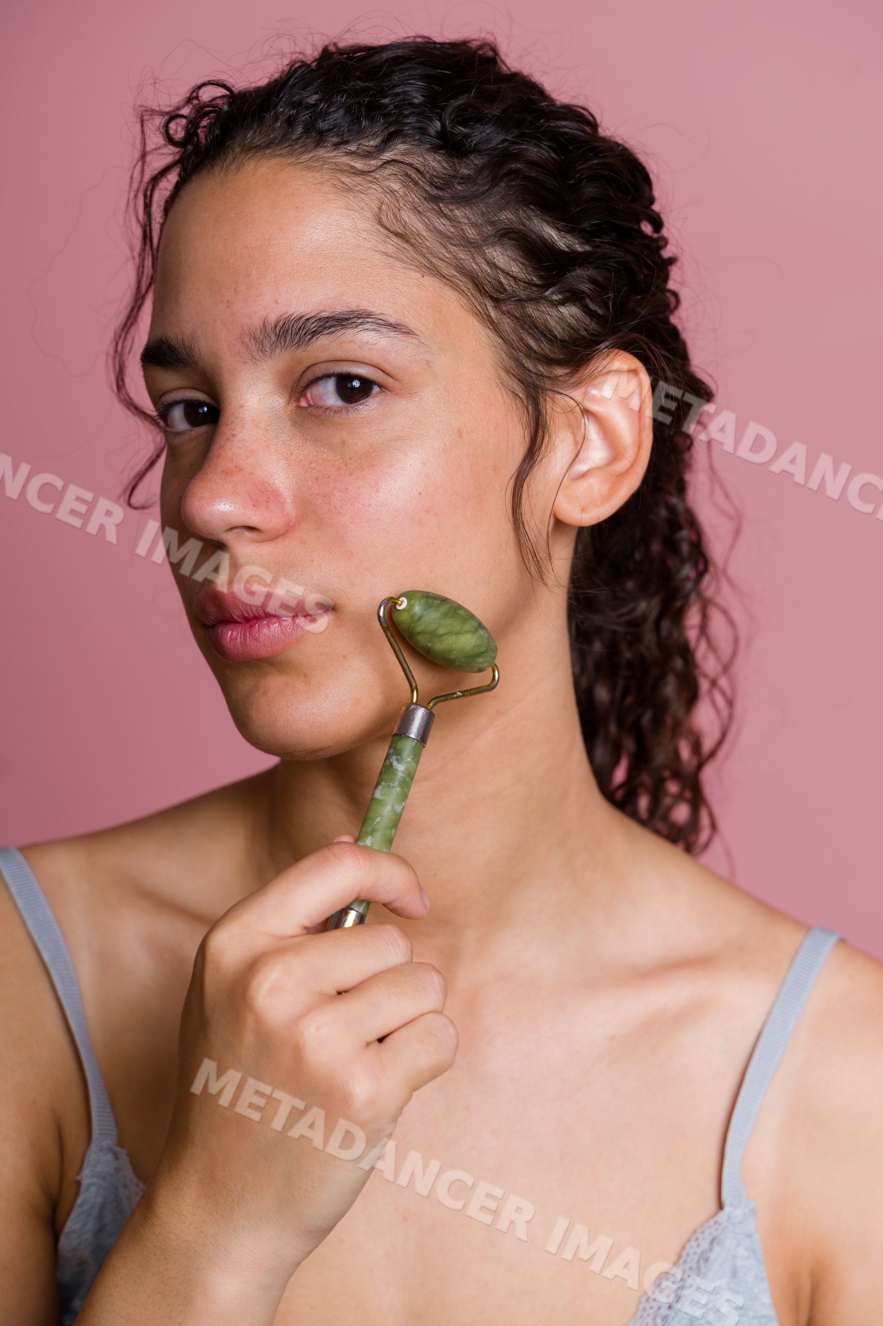 Hispanic woman with jade roller massaging face in beauty shoot