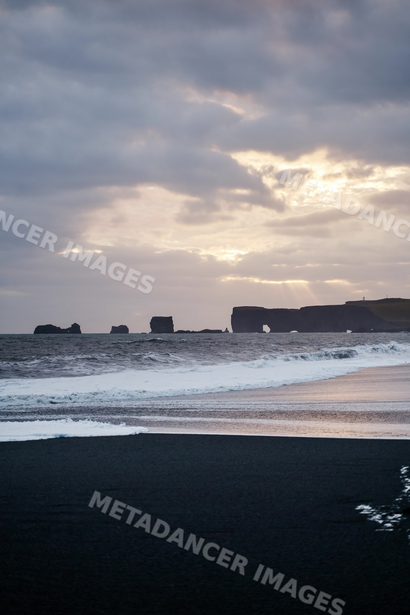 Ocean waves wash ashore on a black sand beach with sea stacks