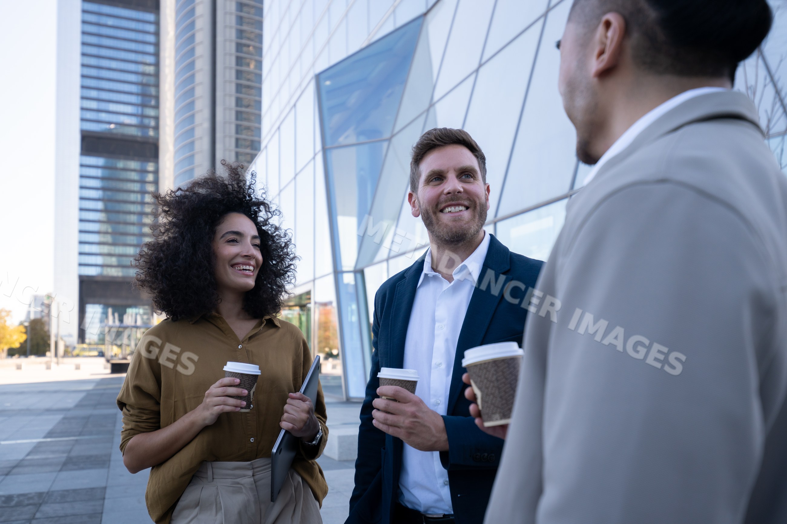 Business colleagues chatting with coffee outside modern office