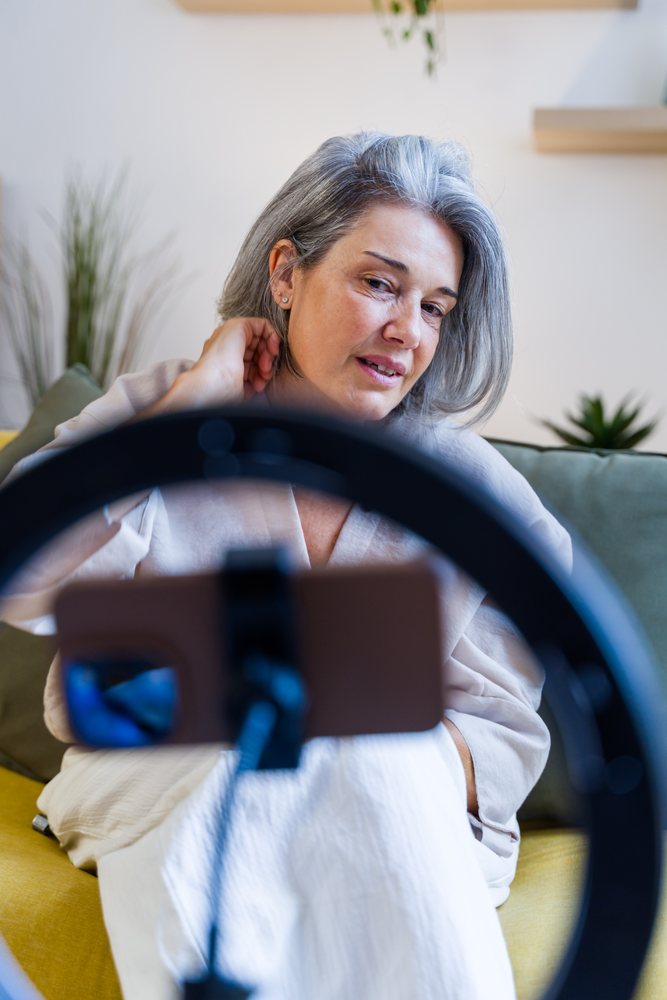 Senior white woman using smartphone with ring light indoors on sofa