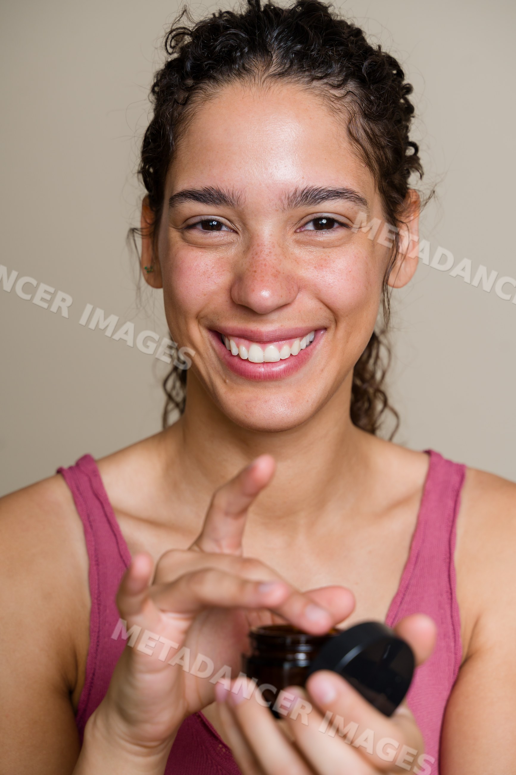 Hispanic woman applying face cream from a brown jar indoors