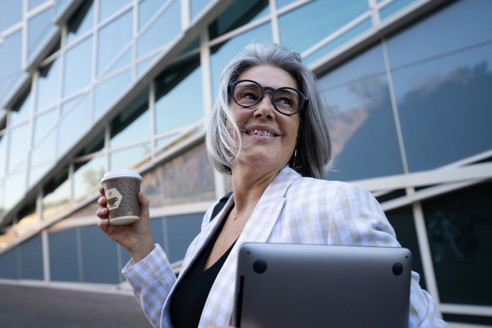 Businesswoman holding coffee cup and laptop outside office building