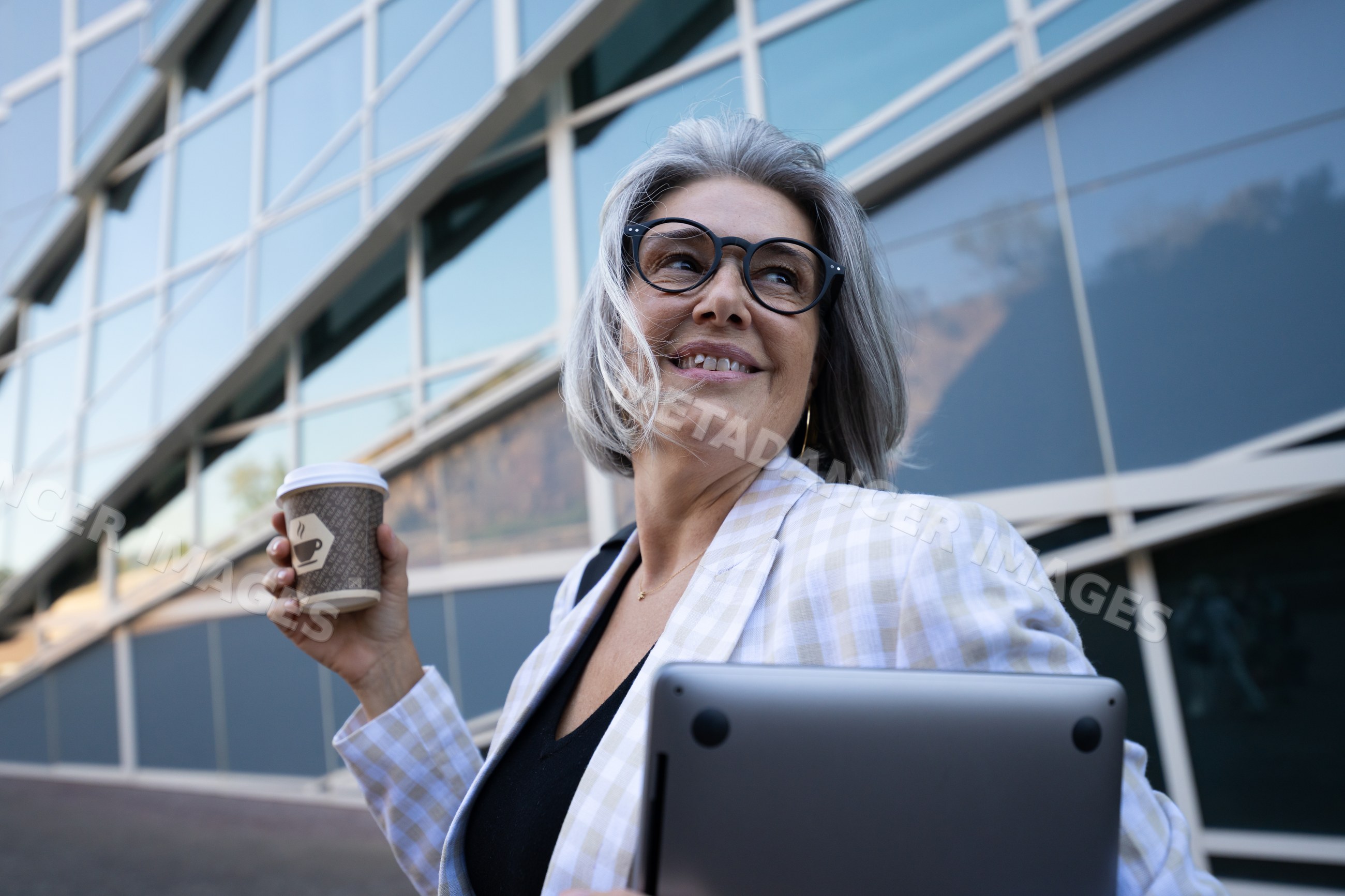 Businesswoman holding coffee cup and laptop outside office building