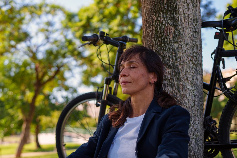 Hispanic woman meditating by tree with bicycle in Málaga park