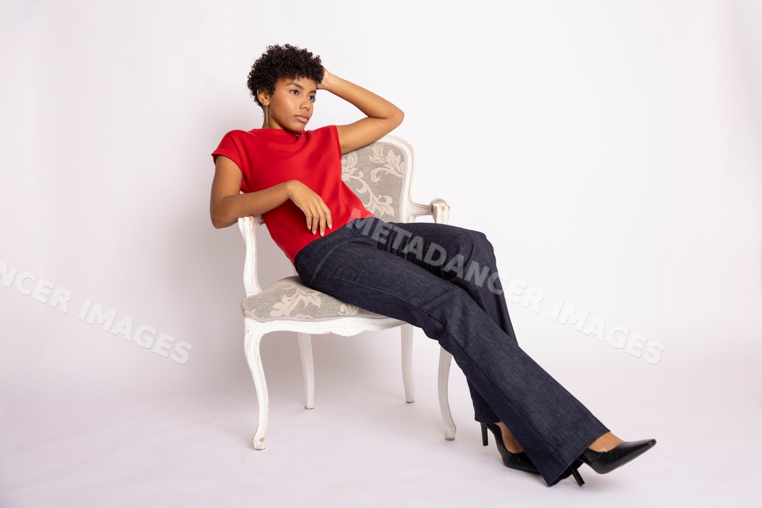 Hispanic woman in red top and blue jeans posing in white chair studio