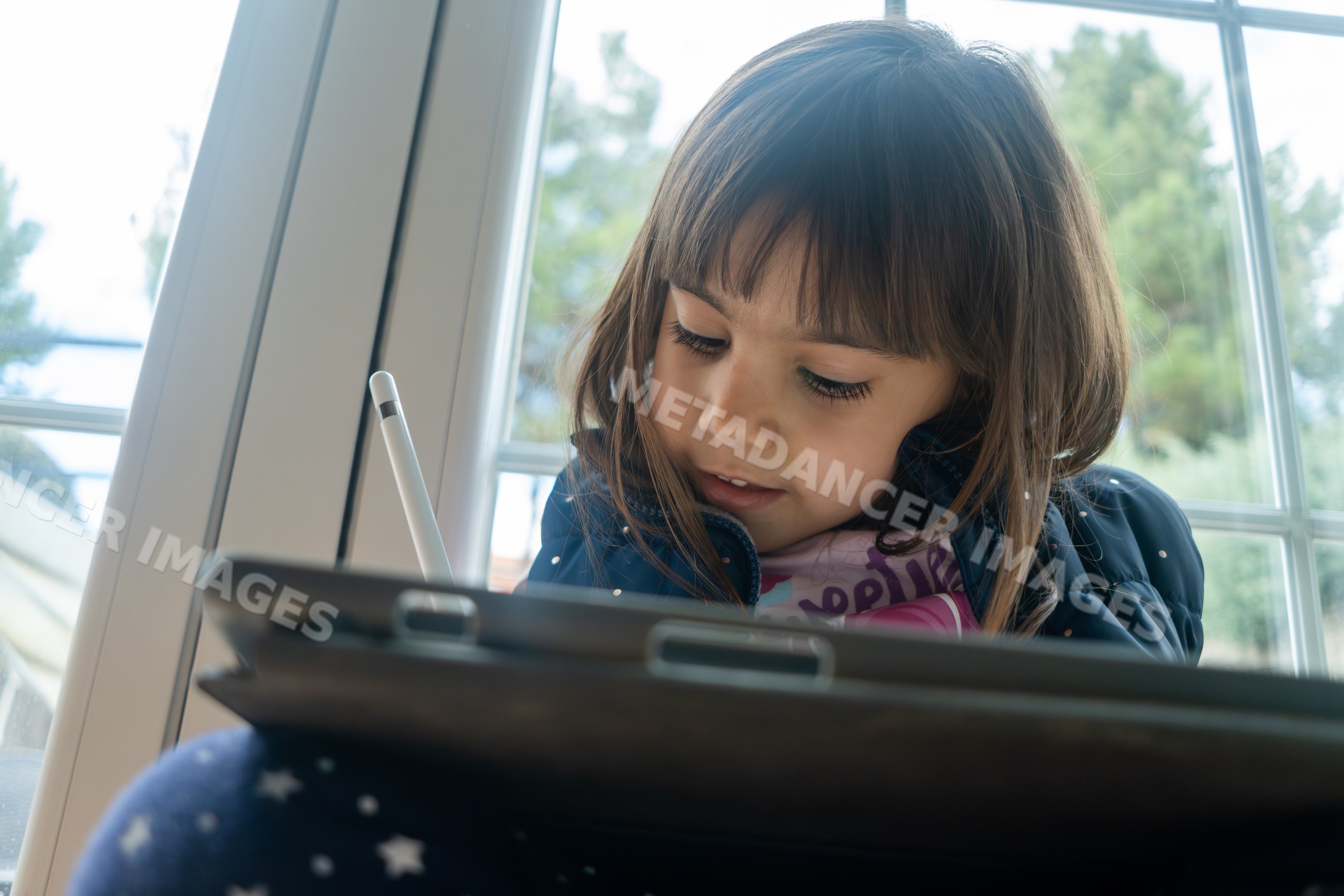 Young white girl using a digital tablet indoors near a window