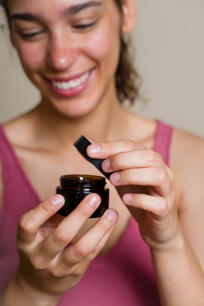 Hispanic woman opening dark cosmetic jar during beauty shoot