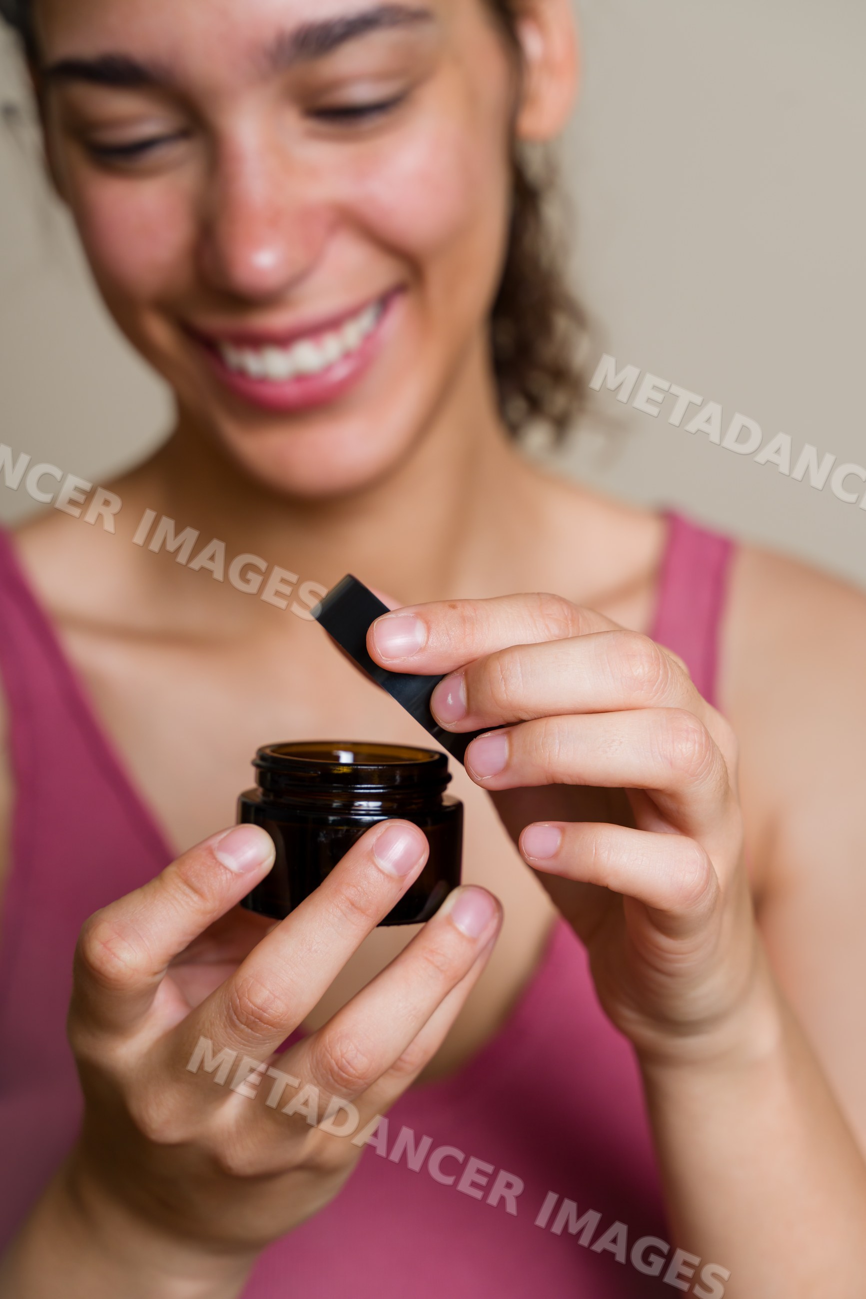 Hispanic woman opening dark cosmetic jar during beauty shoot