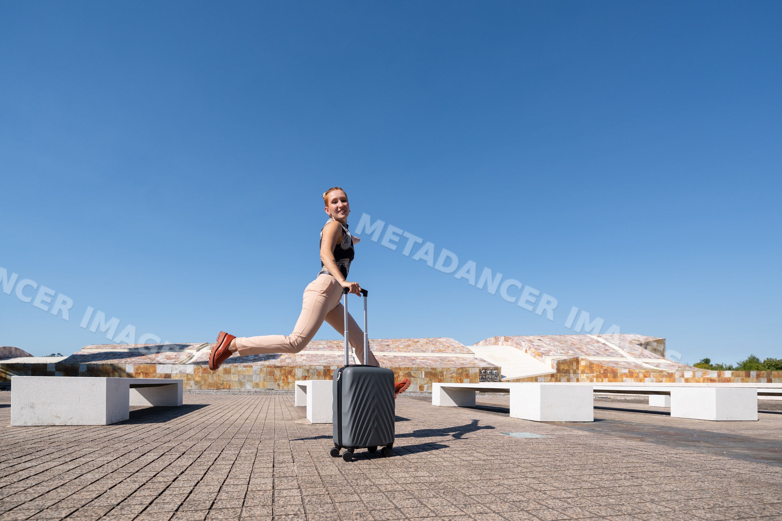 White woman jumping over suitcase in modern plaza in Spain
