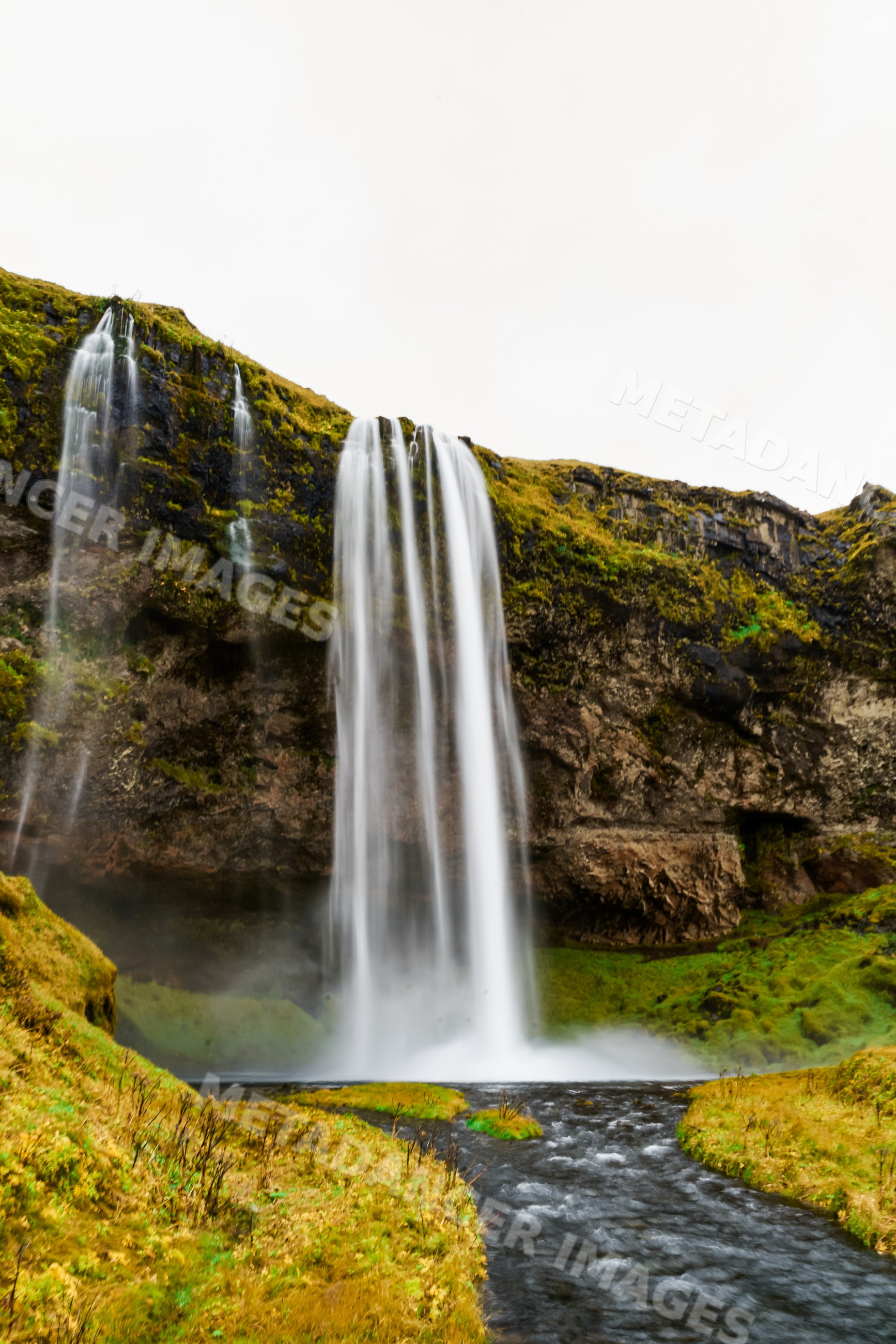A waterfall flows over a mossy cliff into a river