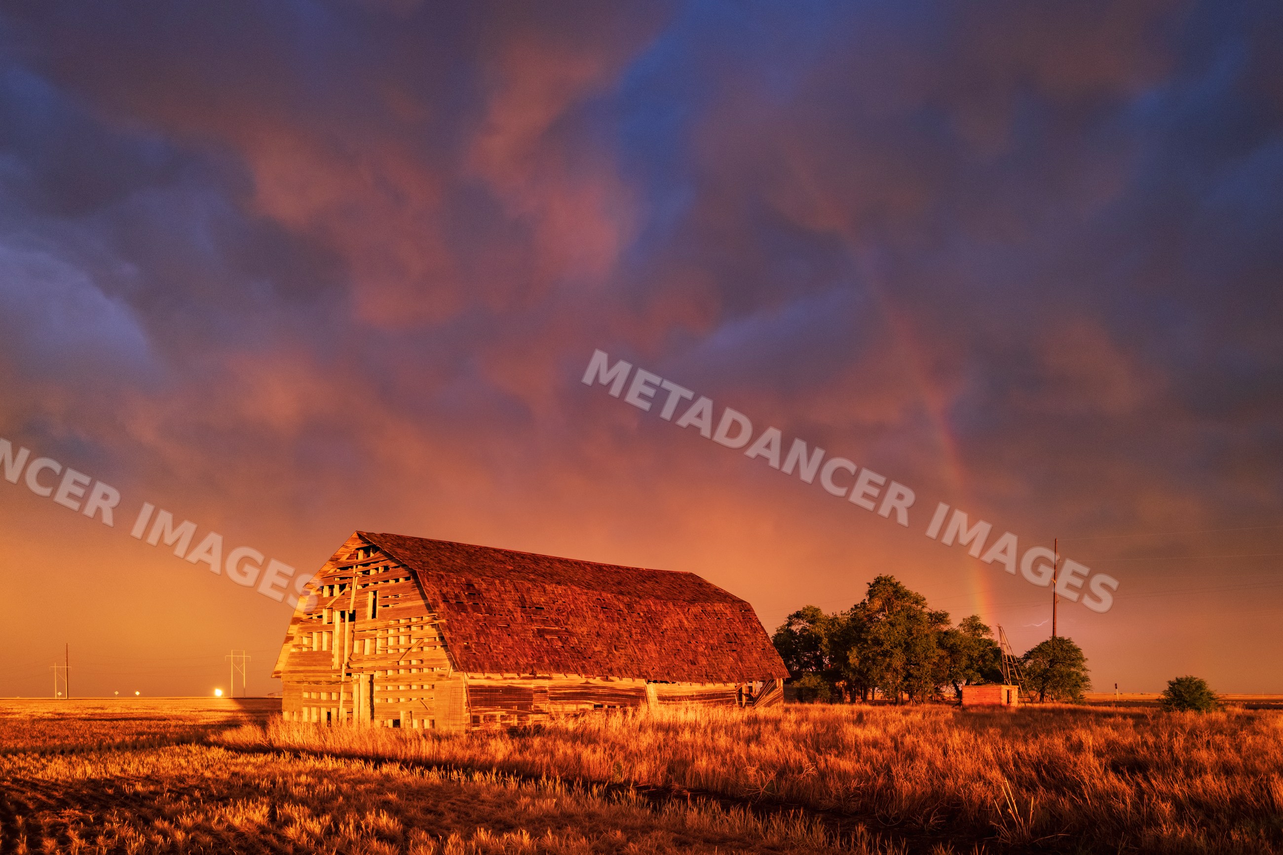 Old barn at sunset with rainbow and storm clouds