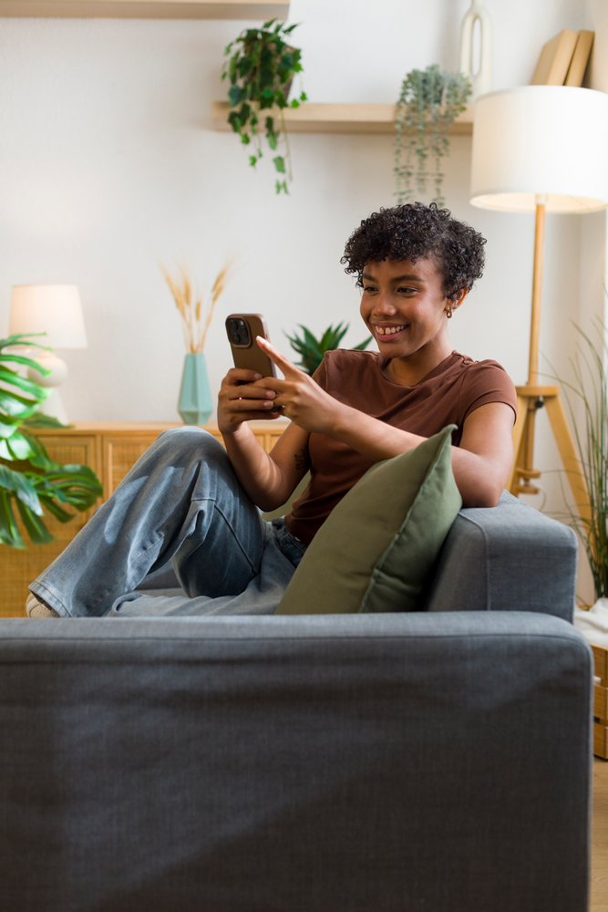 African American woman using smartphone while sitting on sofa indoors