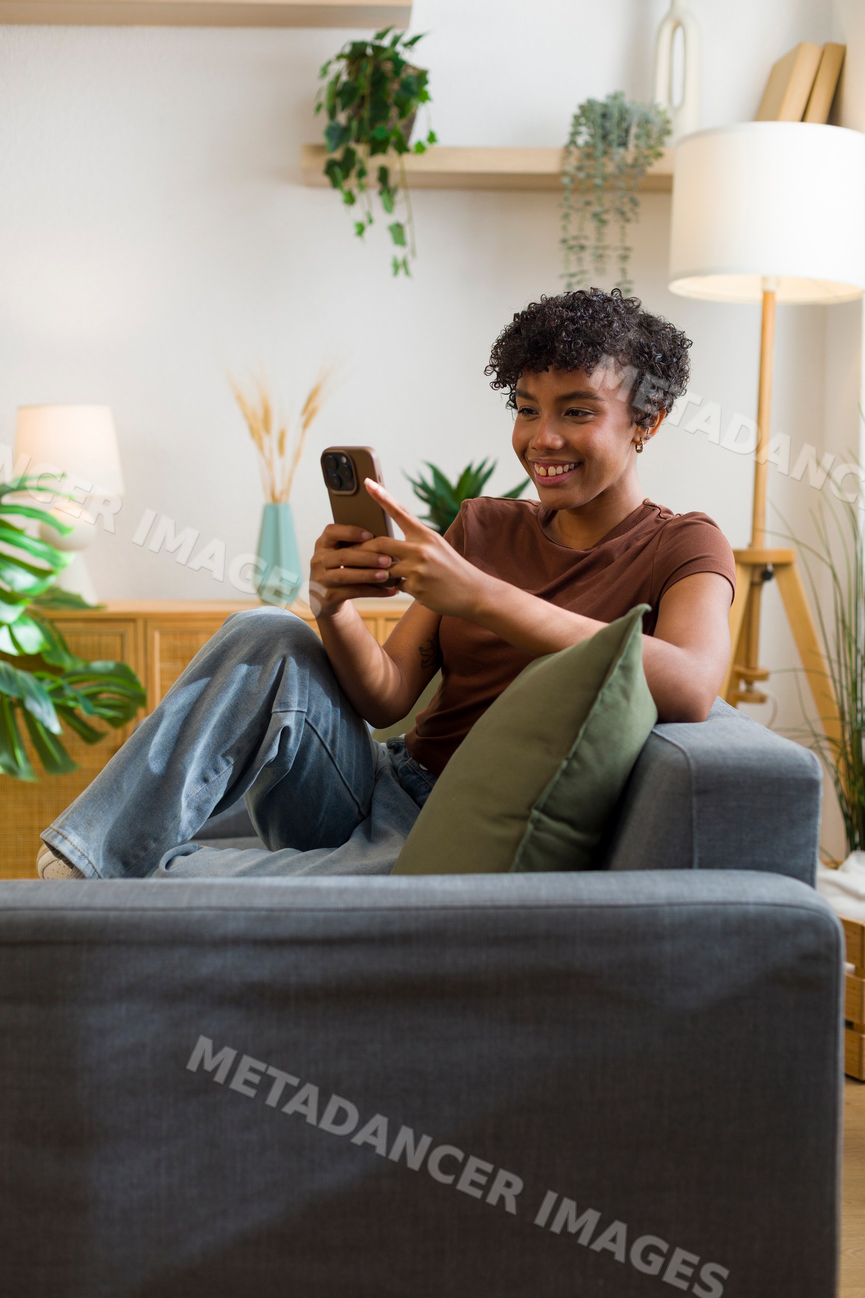 African American woman using smartphone while sitting on sofa indoors