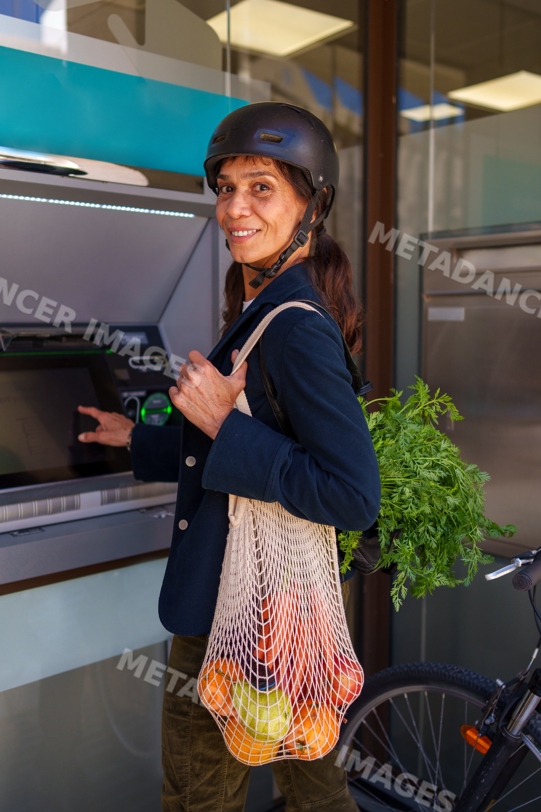 Hispanic woman carrying fresh produce uses atm outdoors