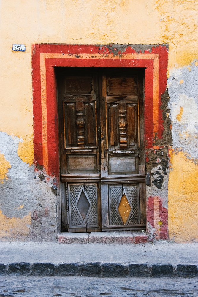 Weathered wooden doorway with red and orange frame on yellow plaster