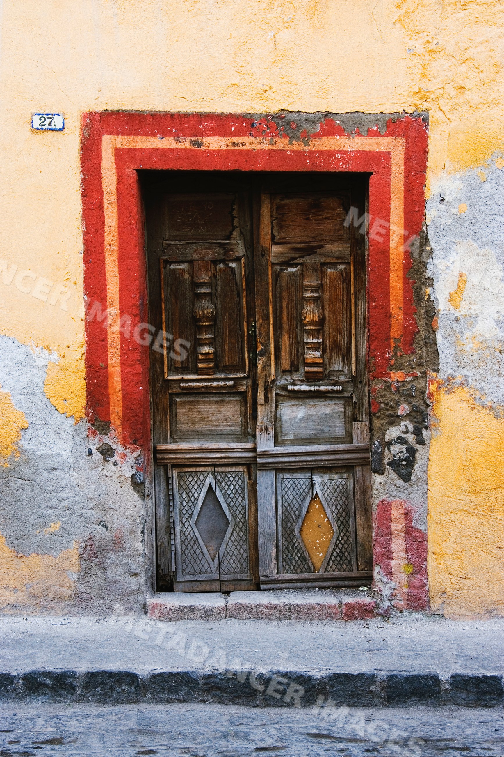 Weathered wooden doorway with red and orange frame on yellow plaster