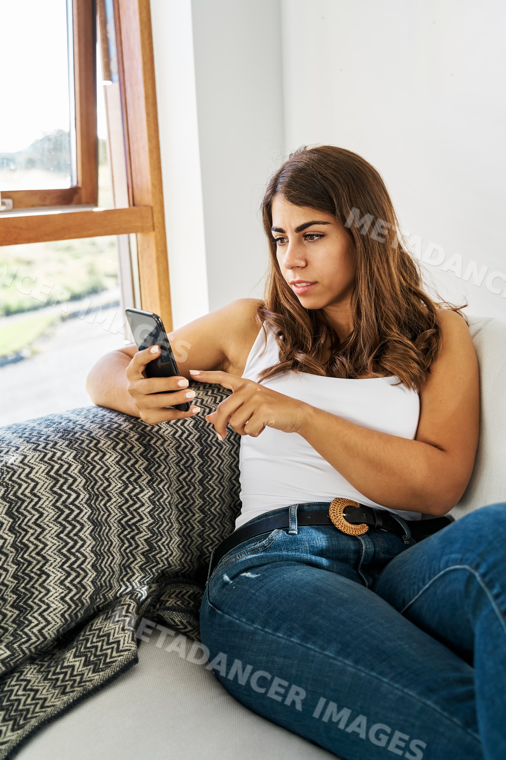 A white woman sitting on a couch using her smartphone indoors