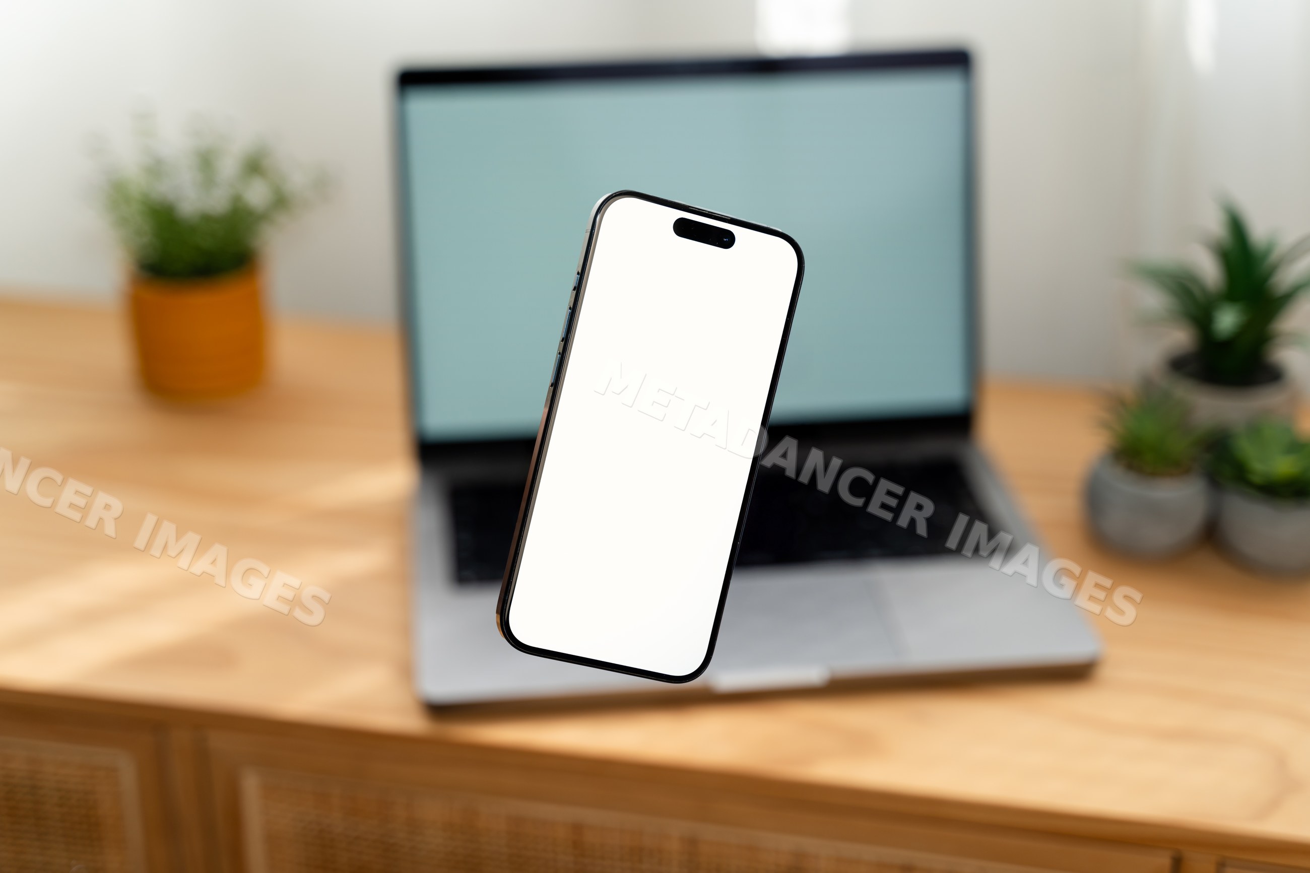 Smartphone floating over desk with laptop and plants in workspace