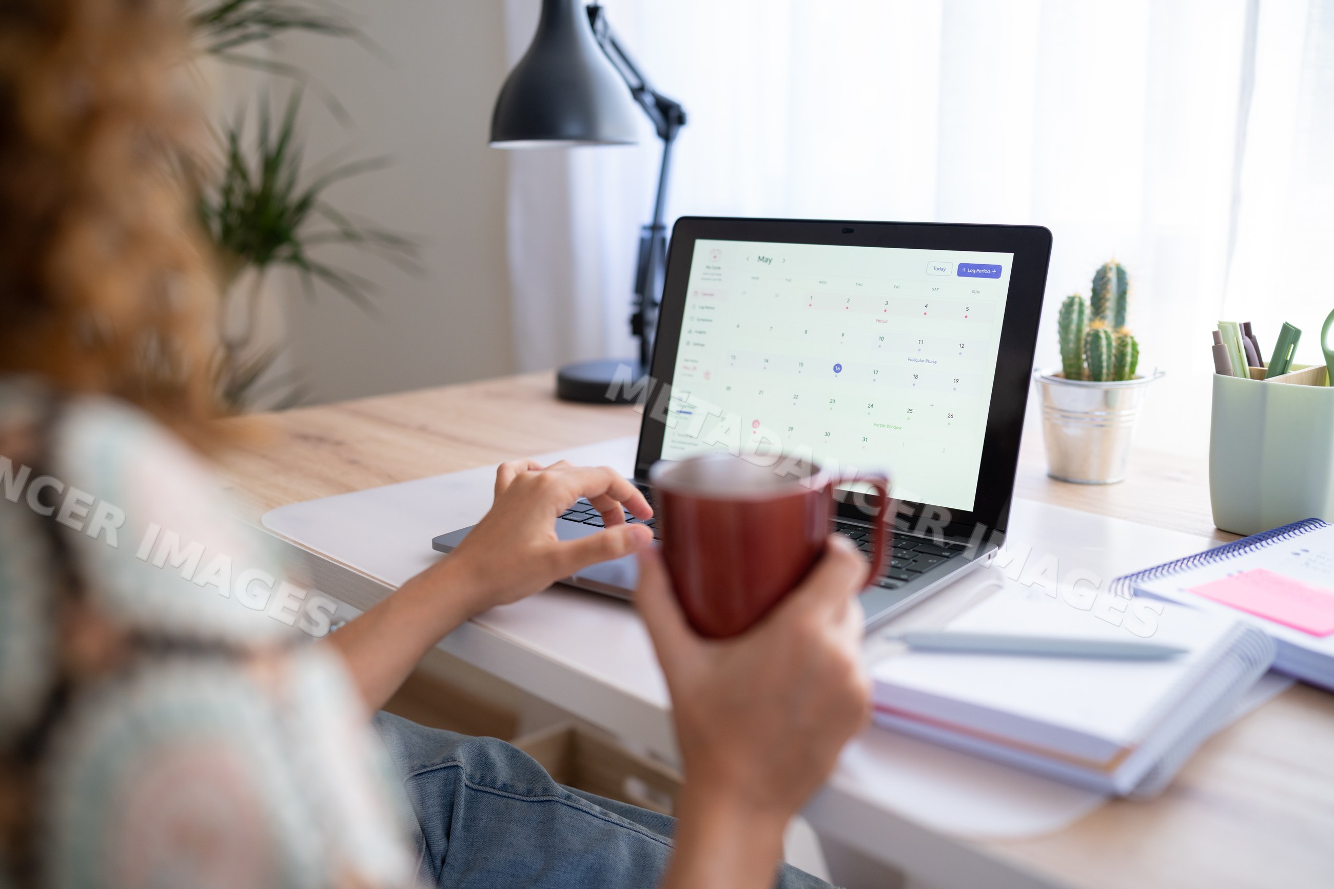 White woman using laptop with calendar and coffee mug