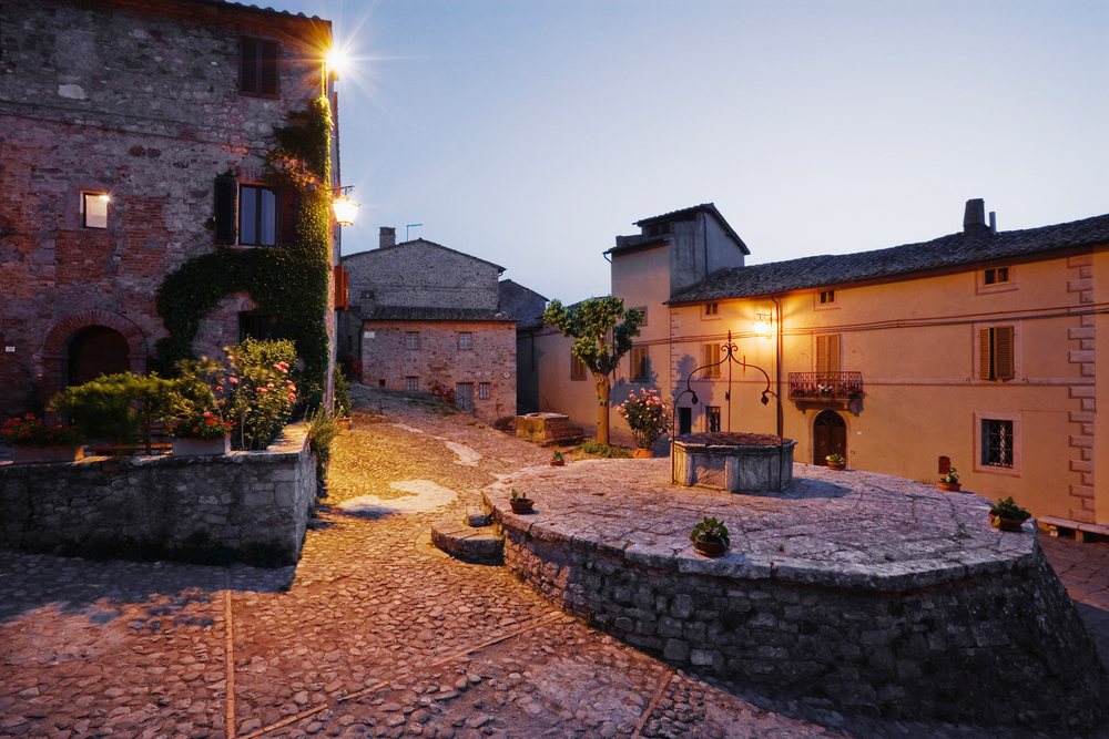 Village square and stone well illuminated at dusk italy