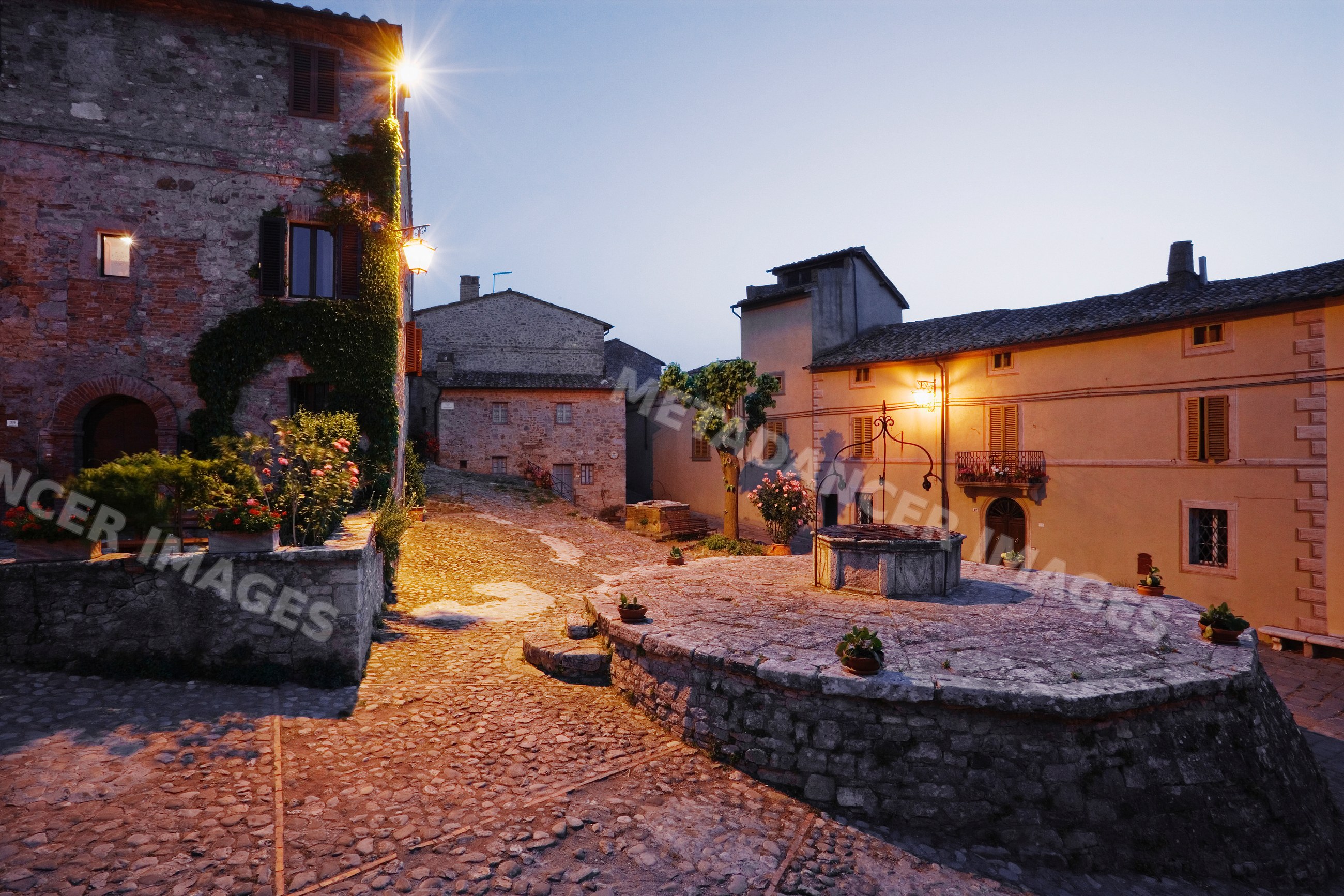 Village square and stone well illuminated at dusk italy