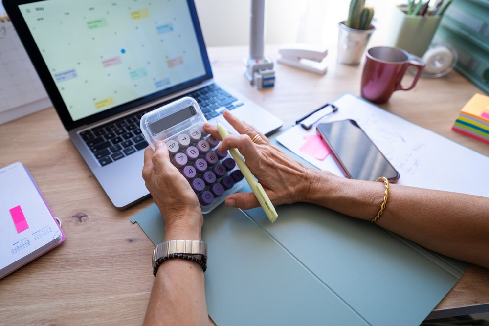 Hands using calculator with laptop calendar and office supplies