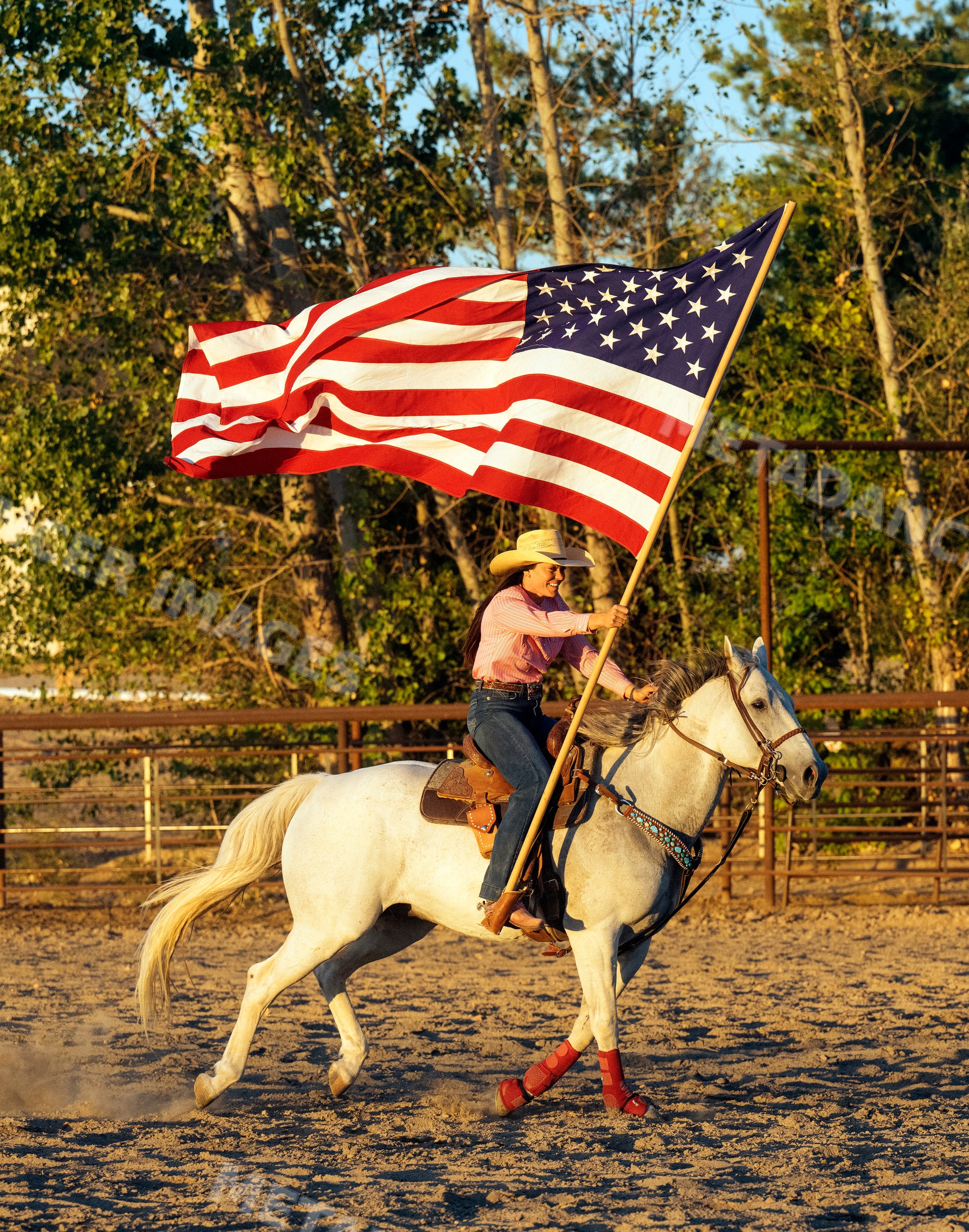Cowgirl riding white horse carrying american flag in outdoor arena