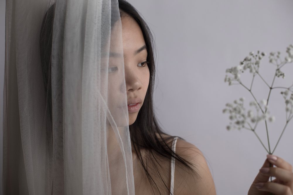 Southeast Asian woman behind sheer curtain holding baby's breath
