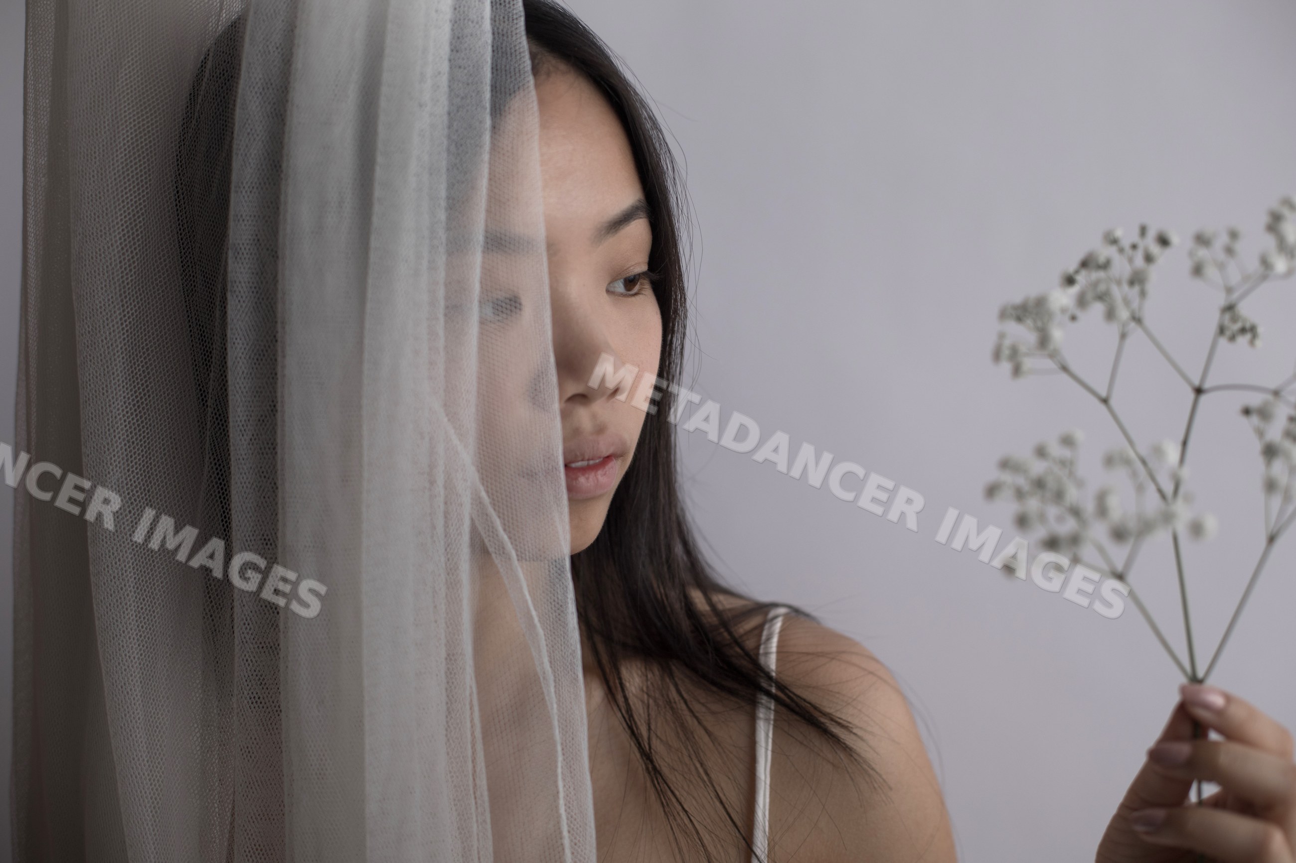 Southeast Asian woman behind sheer curtain holding baby's breath