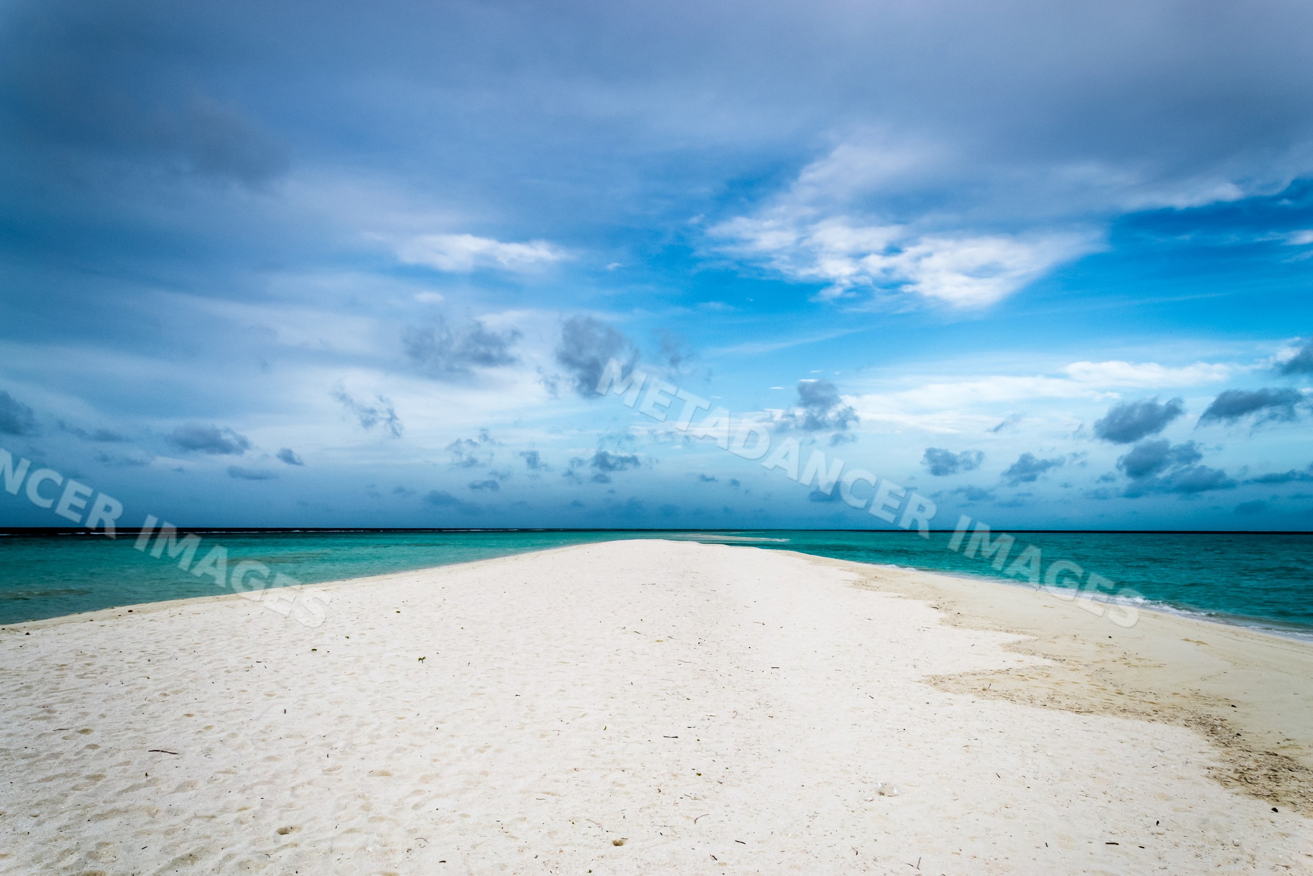 Sandbar extending into turquoise ocean under cloudy sky