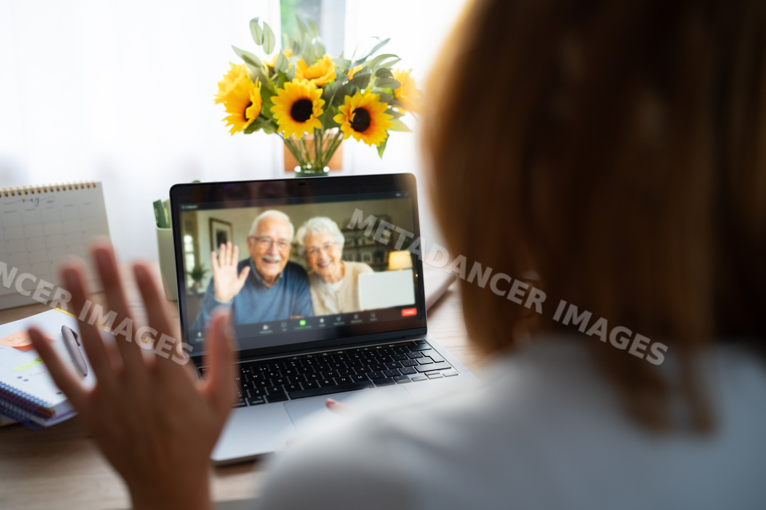 A white woman waves at a senior couple during a video call at home