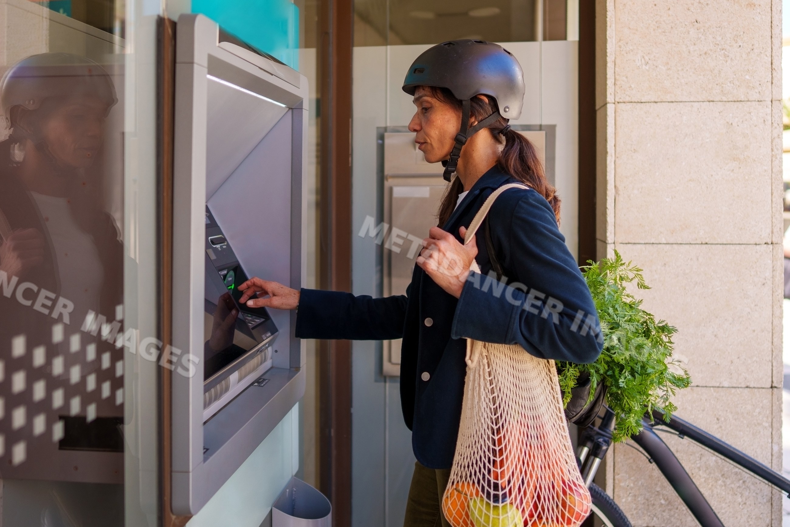 Hispanic woman using outdoor atm with groceries beside bike