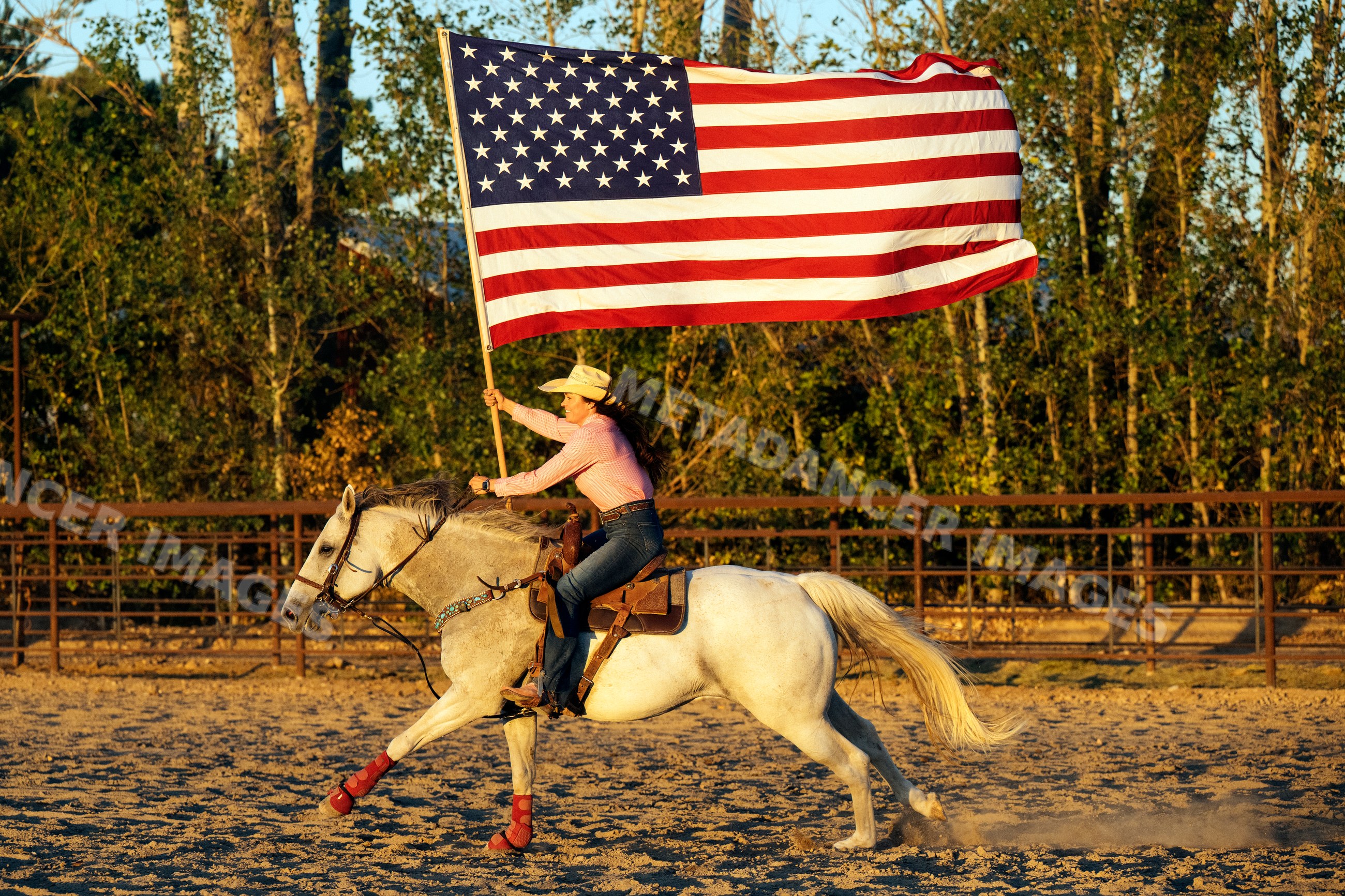 Woman riding white horse waving american flag in horseriding arena