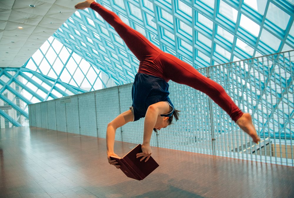 A woman performs a handstand holding a book