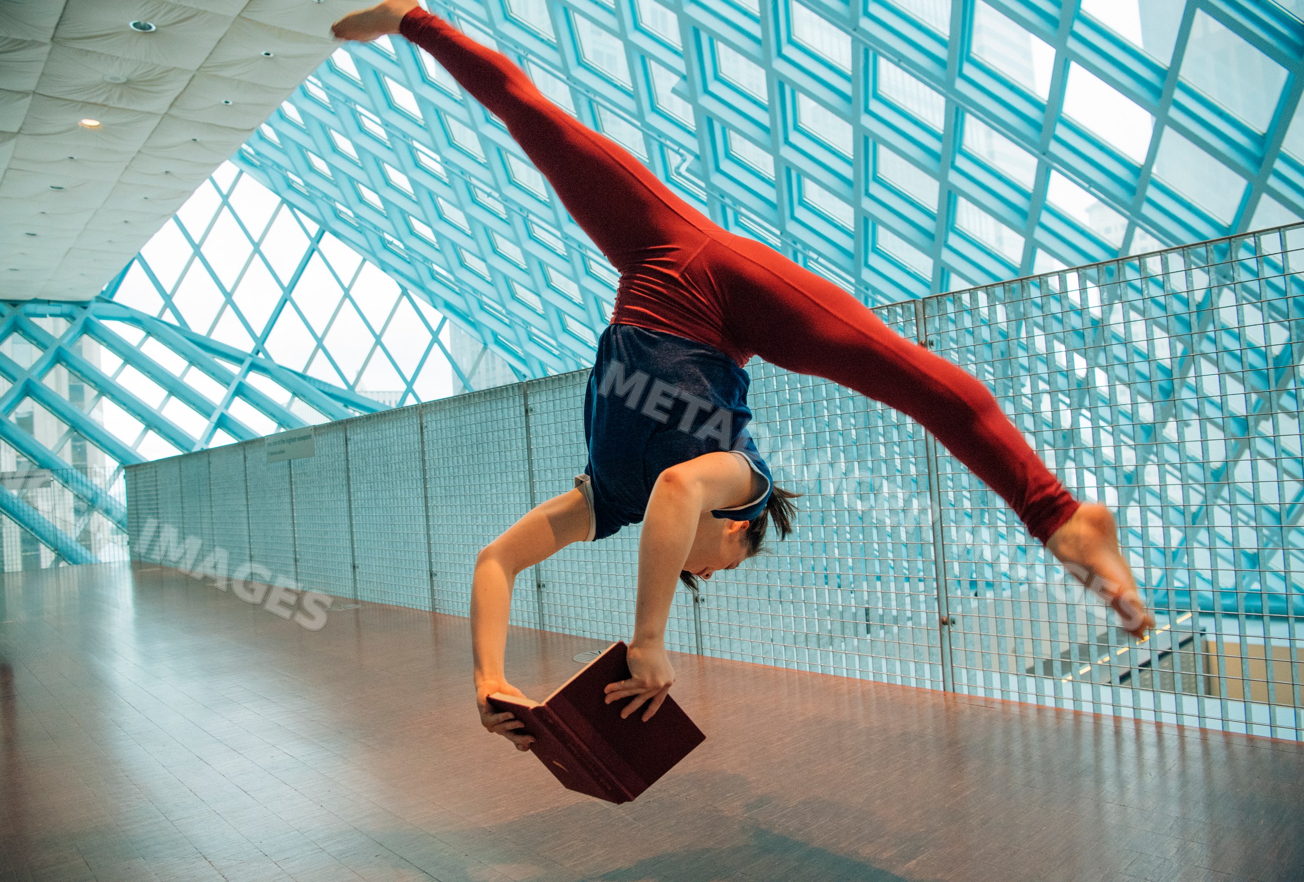 A woman performs a handstand holding a book