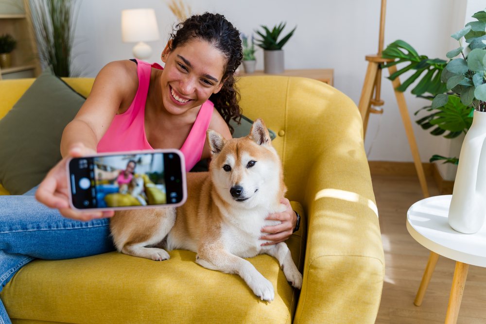 A Hispanic woman happily takes a selfie with her dog