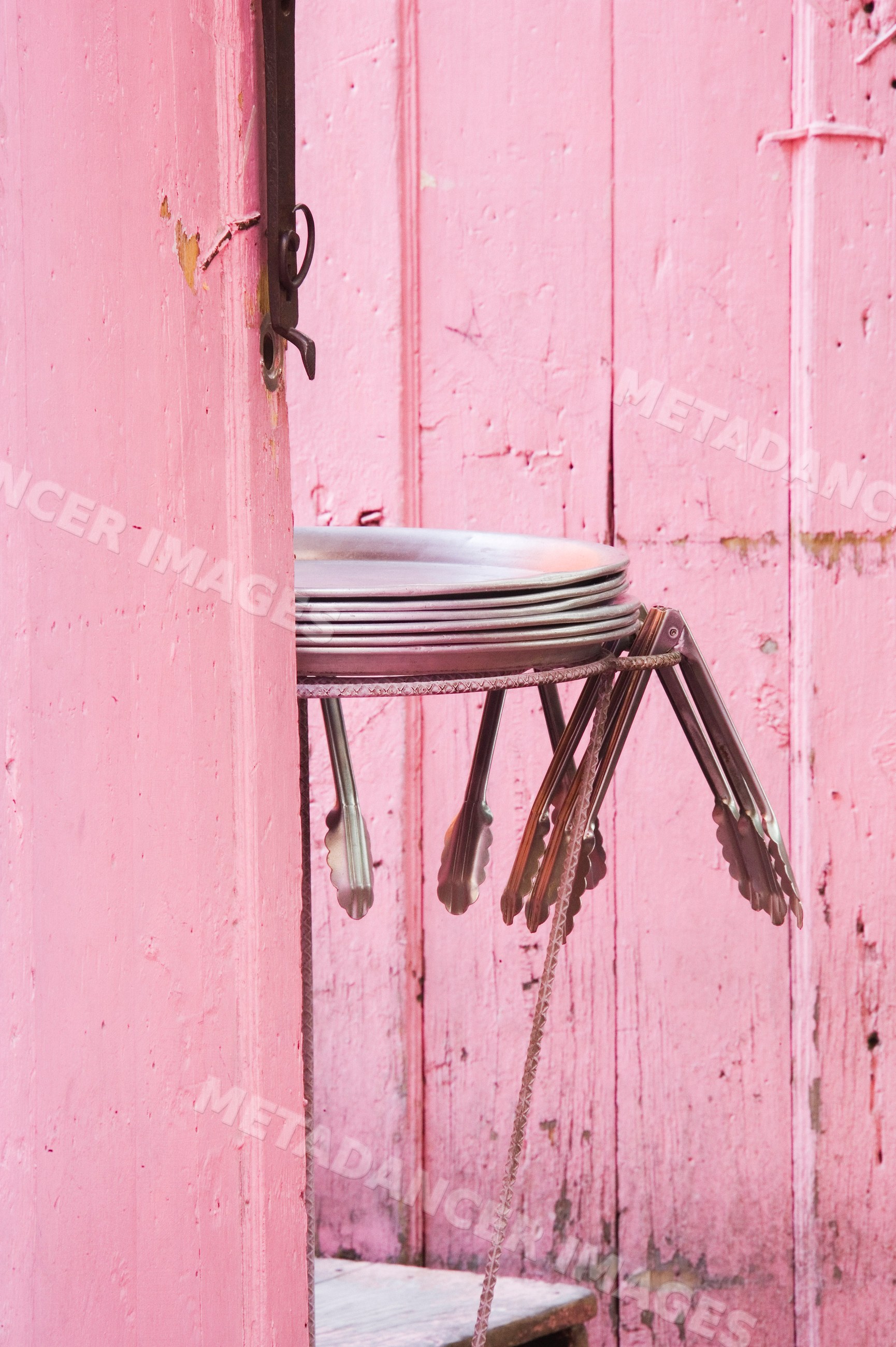 Metal trays and tongs hanging behind rustic pink wooden door, mexico