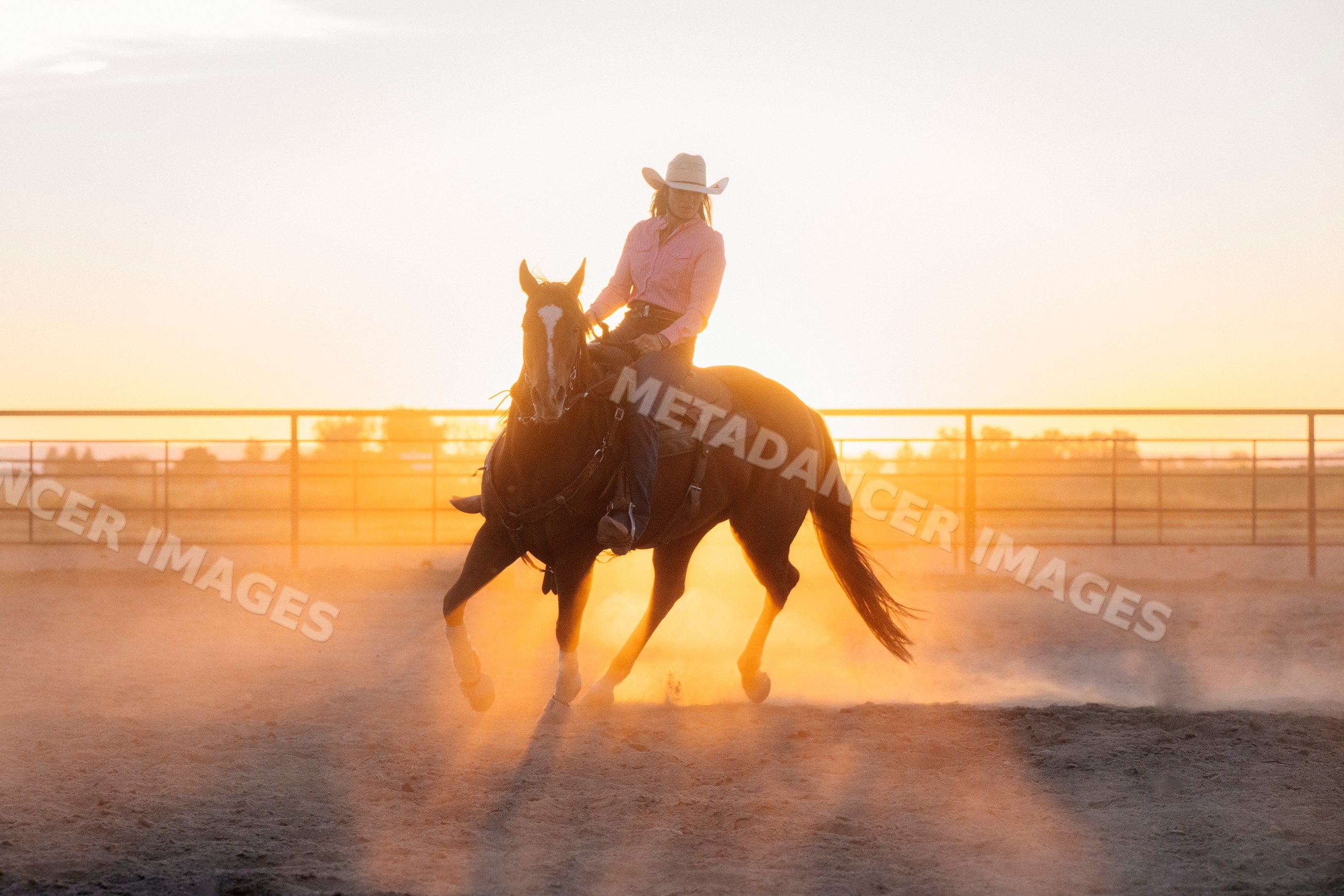 White woman riding a horse in a dusty arena at Southwest USA sunset