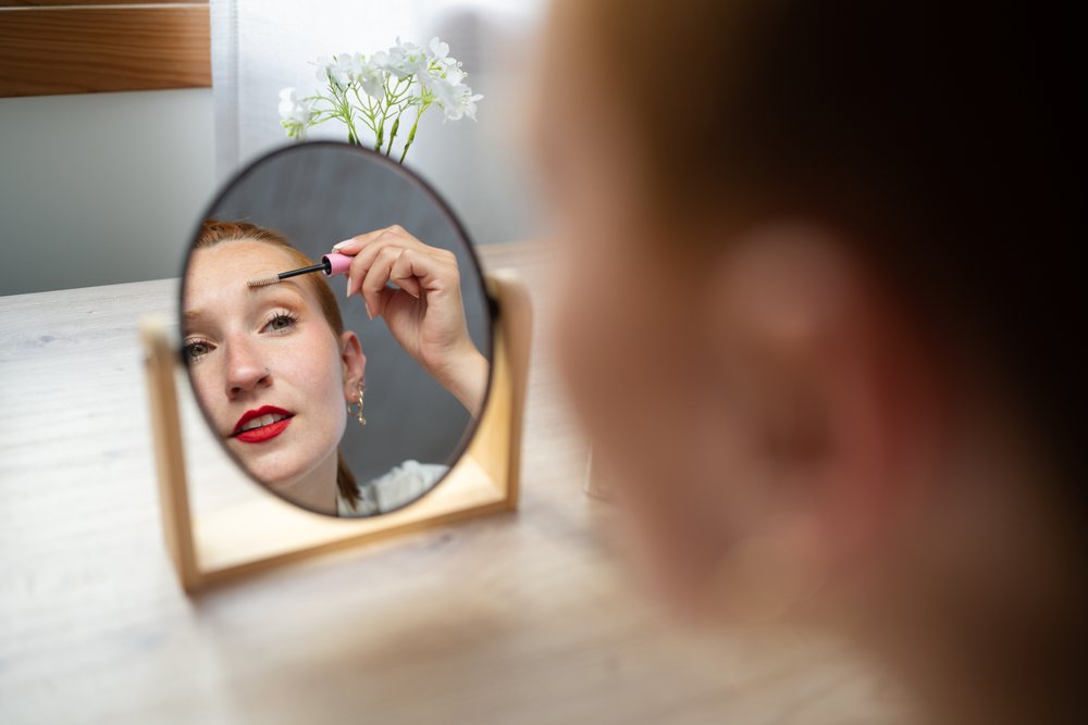 A white woman applies mascara looking