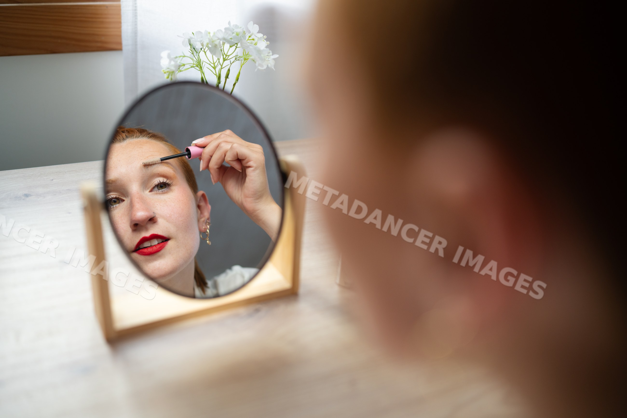 A white woman applies mascara looking