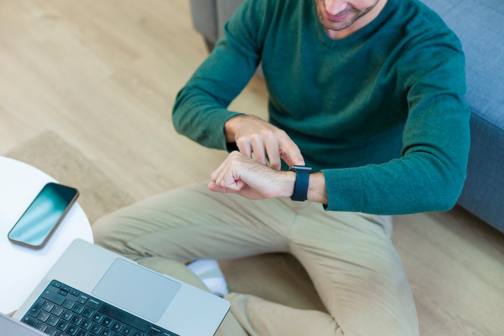 White man checking smart watch while sitting cross-legged on floor