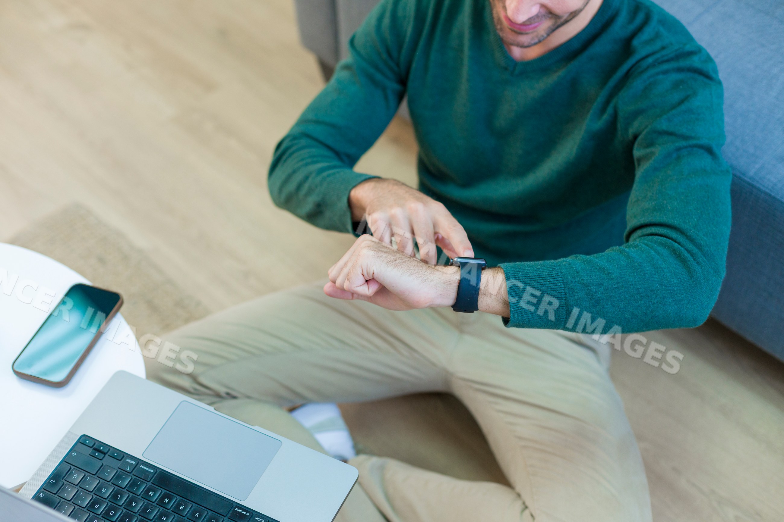 White man checking smart watch while sitting cross-legged on floor