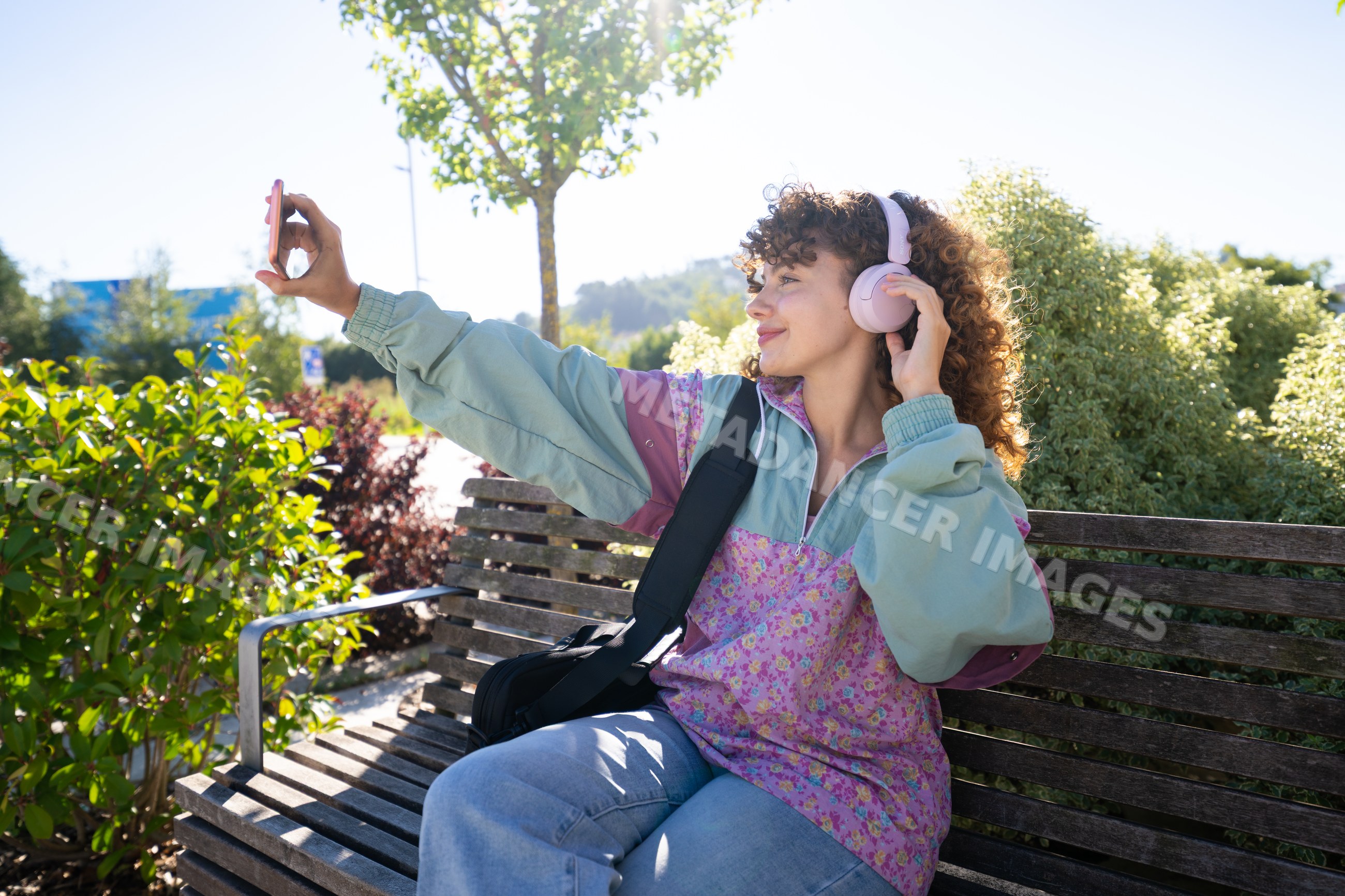 White woman taking selfie with pink headphones on wooden bench