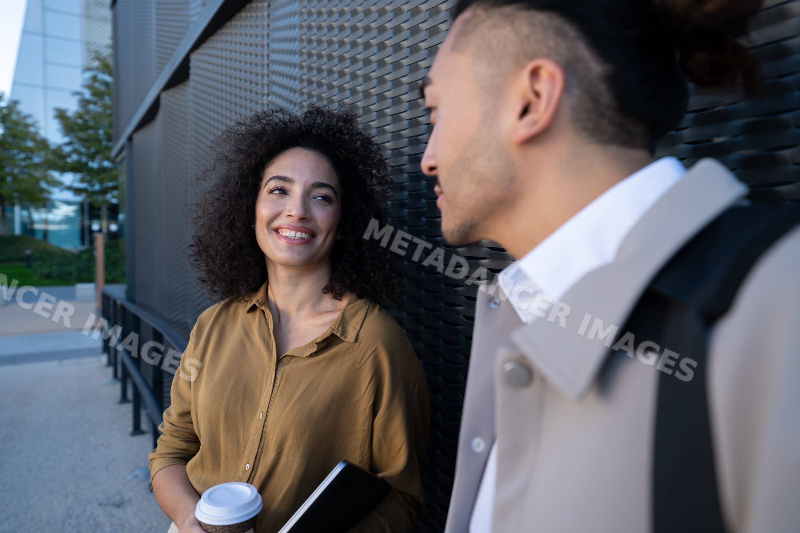 Two people having a conversation outdoors beside black metal wall
