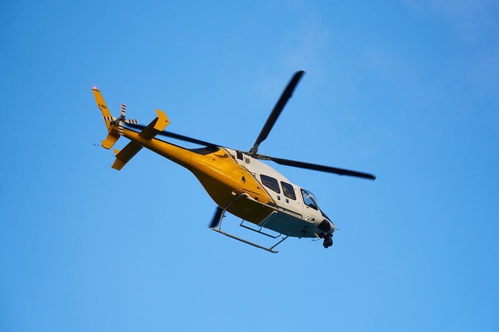 Yellow and white helicopter flying in clear sky