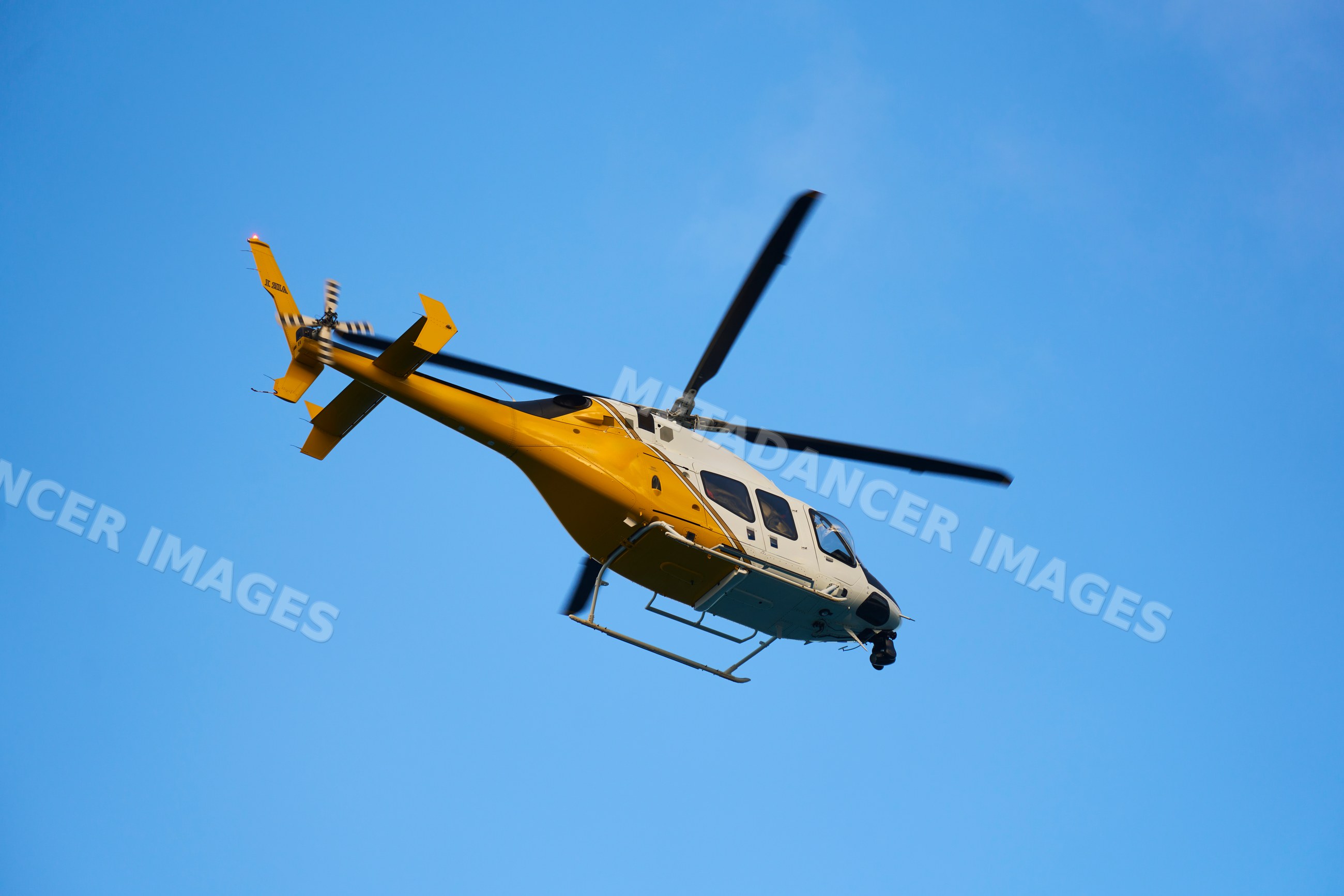 Yellow and white helicopter flying in clear sky